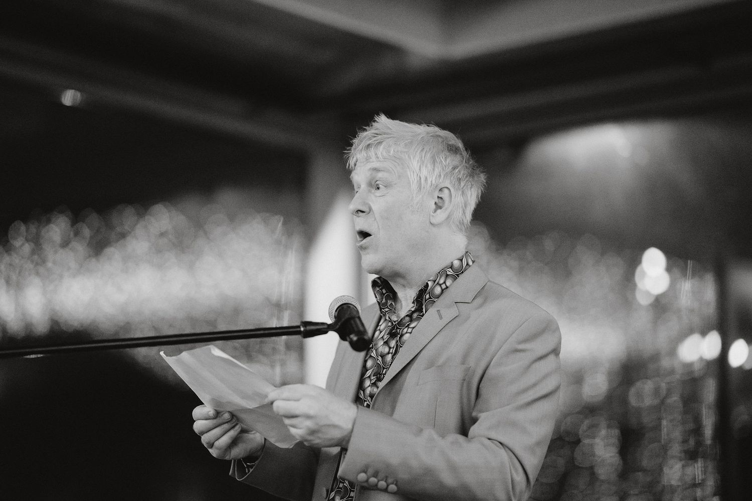 A person performs passionately at a microphone while smoke fills the air in a dimly lit venue.