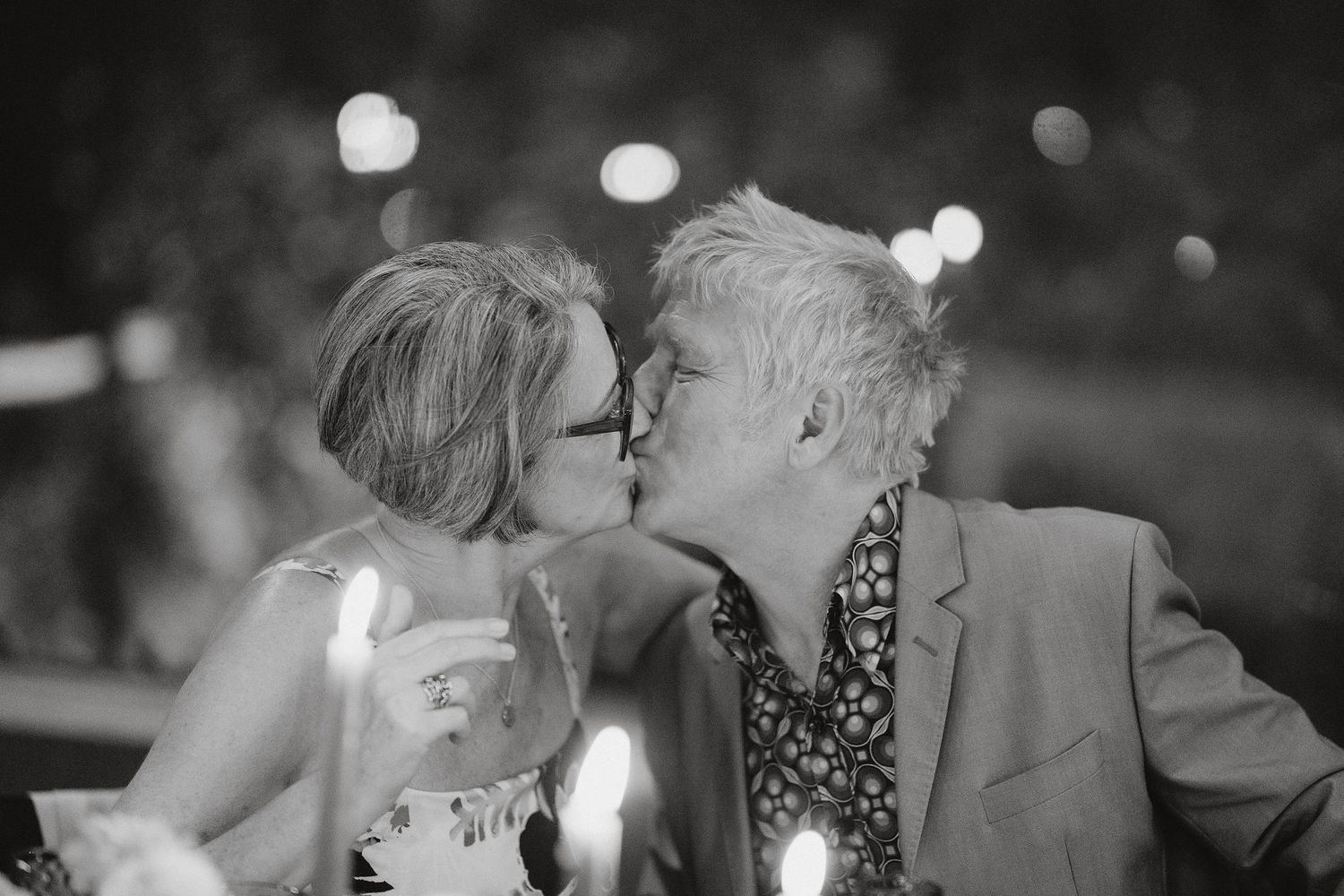 A romantic monochrome moment captured at a nighttime celebration with bokeh lights in the background.