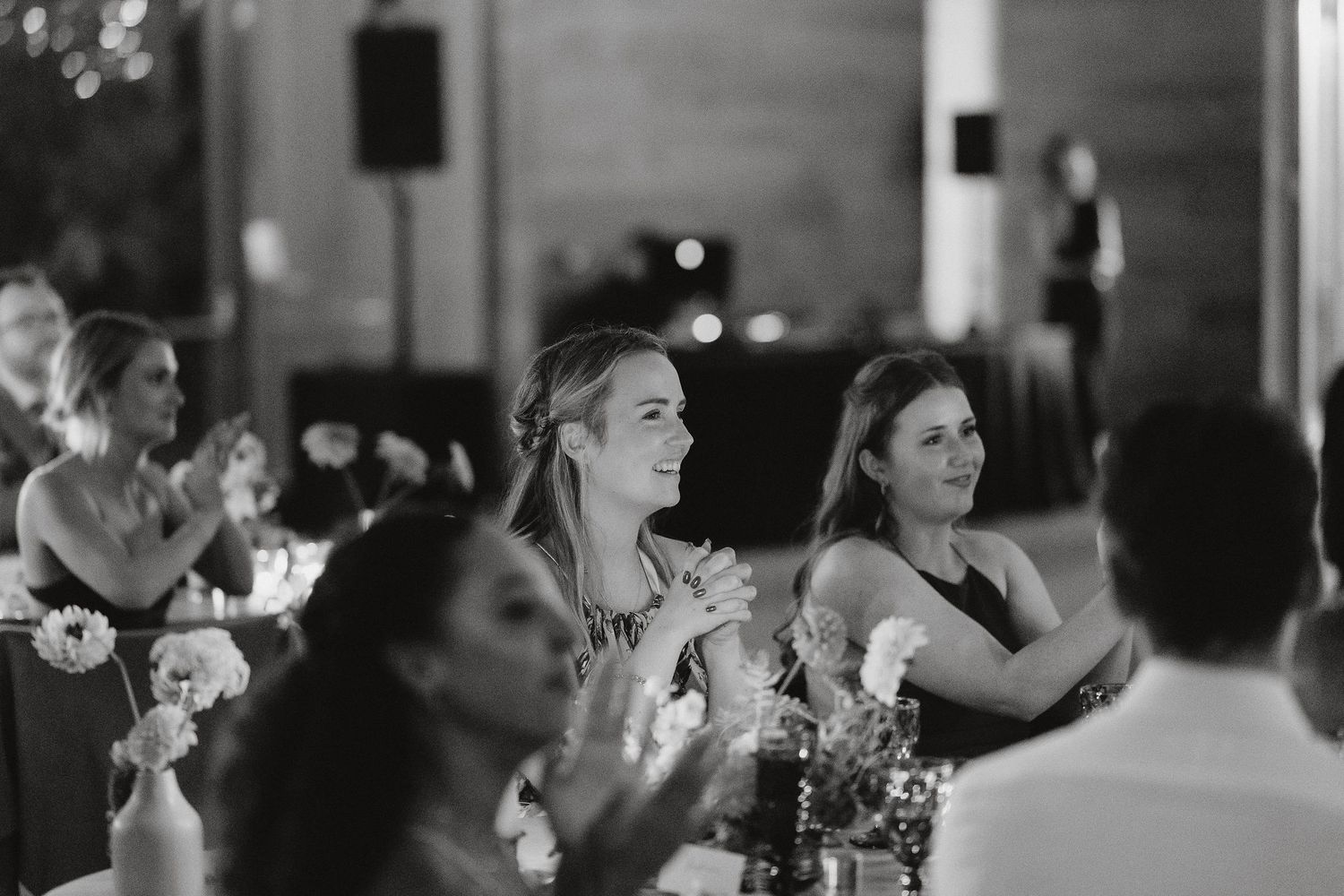 Black and white photo of wedding guests laughing and clapping during a reception celebration.
