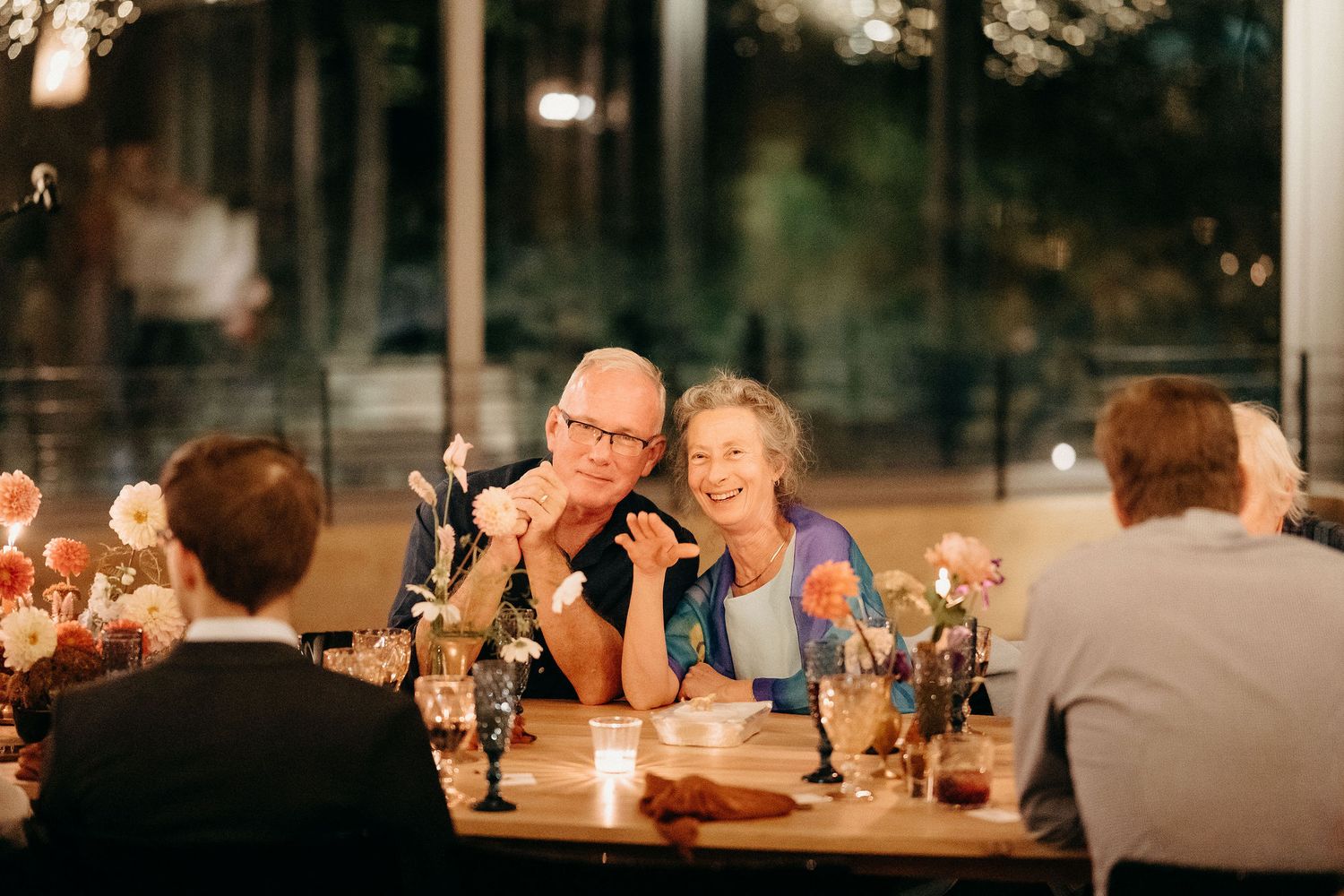 A candid moment captured during an intimate dinner party with guests seated at a wooden table with wine glasses and candles.