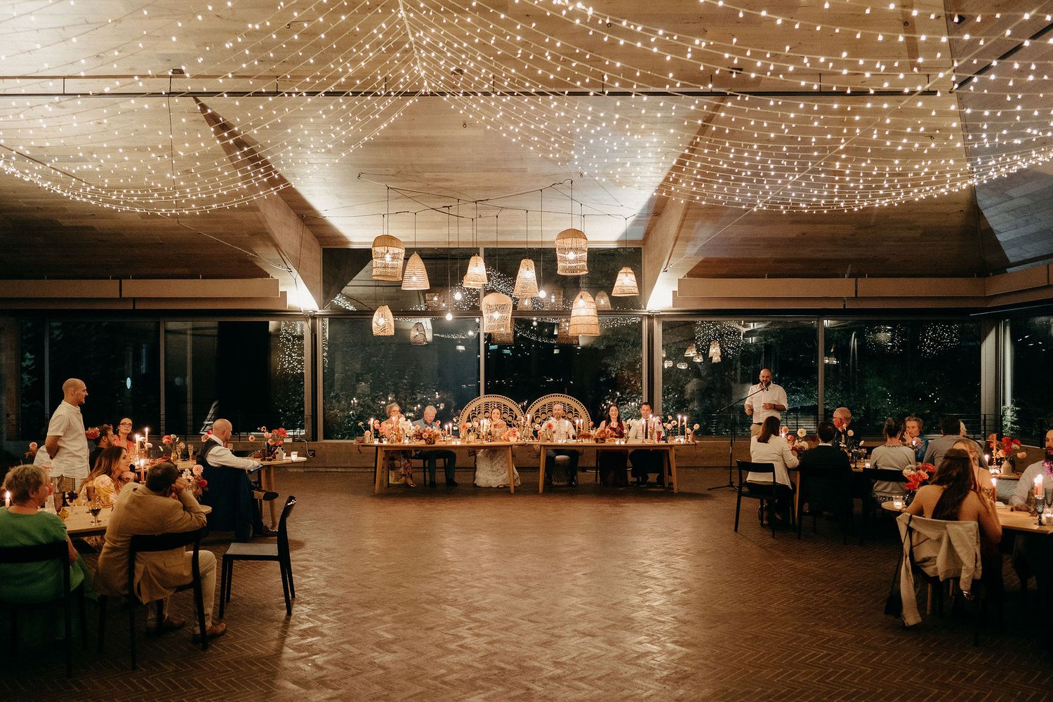 Wedding reception venue with twinkling string lights overhead and guests seated at tables in a warm, romantic atmosphere.