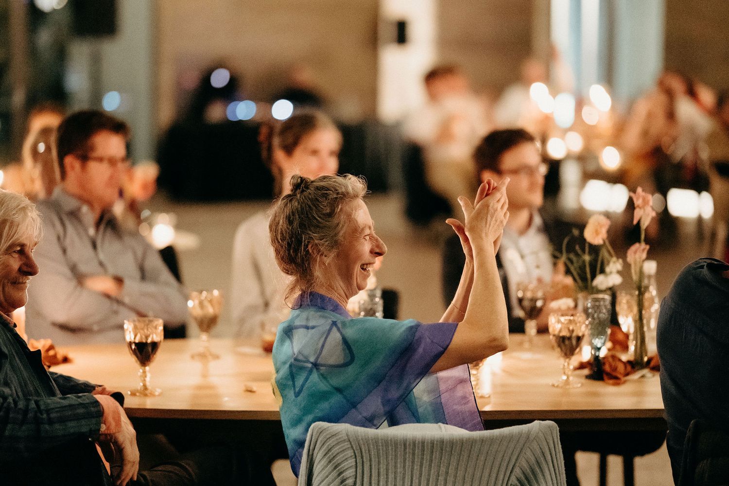 People enjoying dinner and conversation at a candlelit restaurant table in warm ambient lighting.
