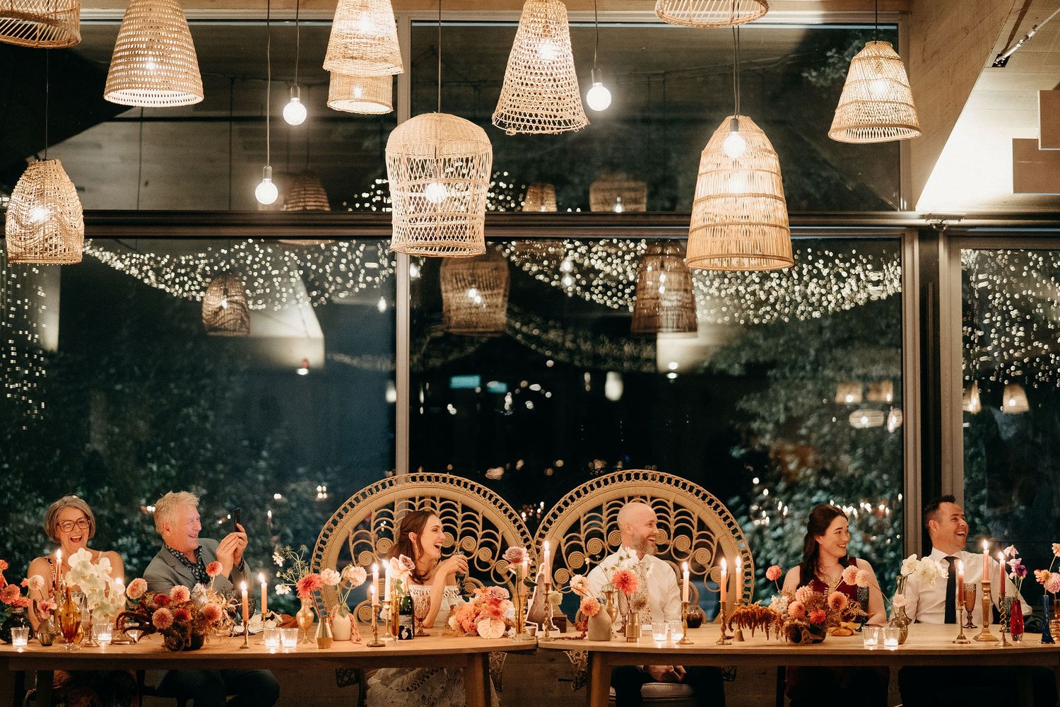 Wedding reception dining table with string lights and wicker pendant lamps creating a warm, romantic atmosphere.