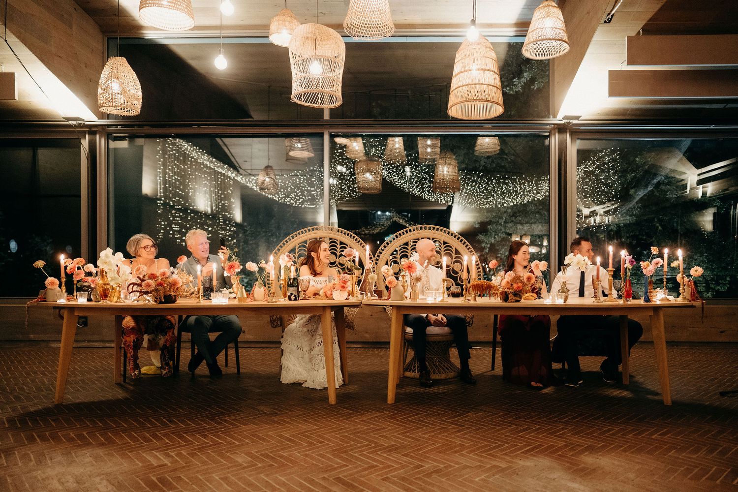 Wedding reception dinner at a rustic venue with hanging lanterns and long wooden tables decorated with floral arrangements.