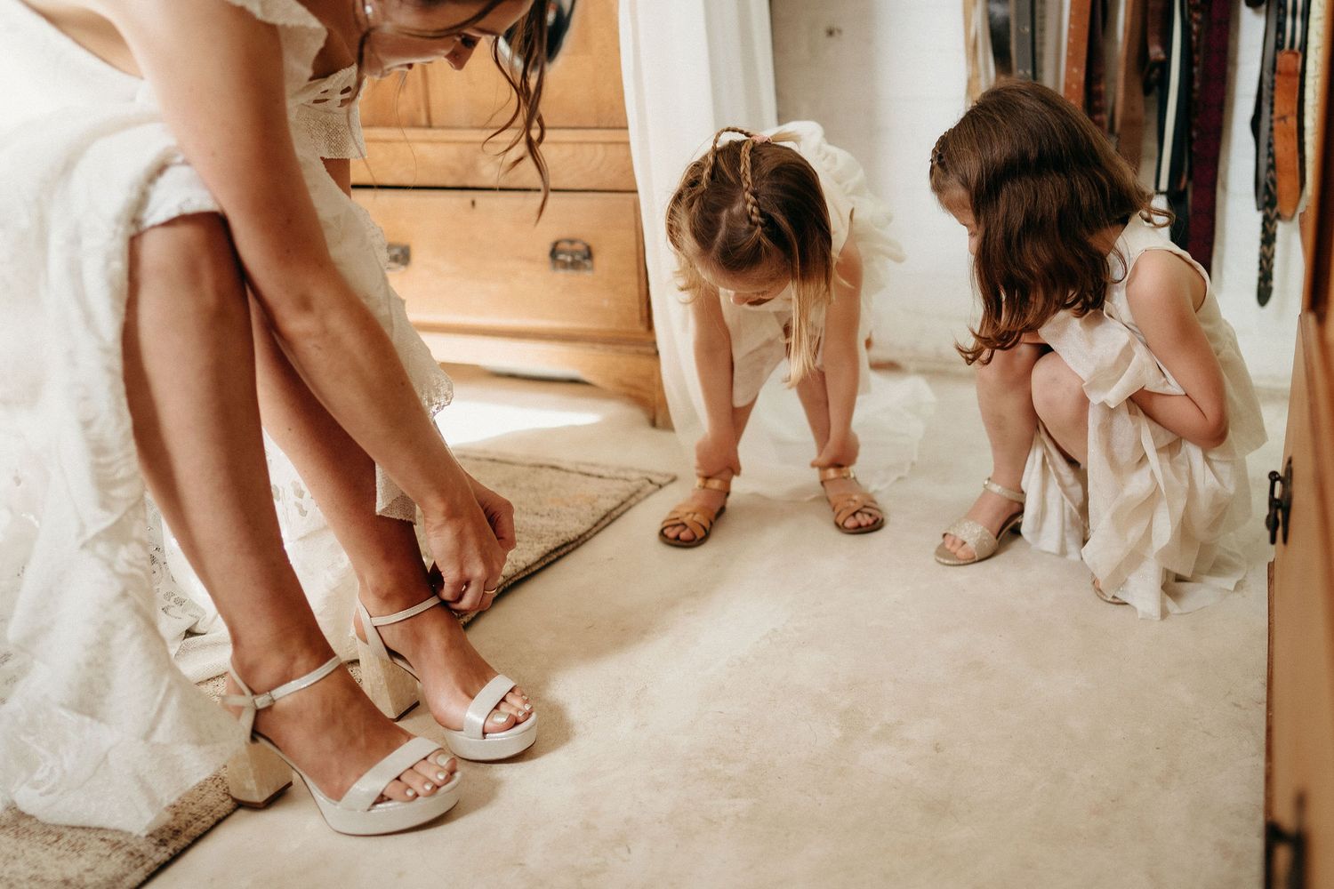 Wedding attendants put on sparkly heels and sandals while getting ready in a room with beige carpet.