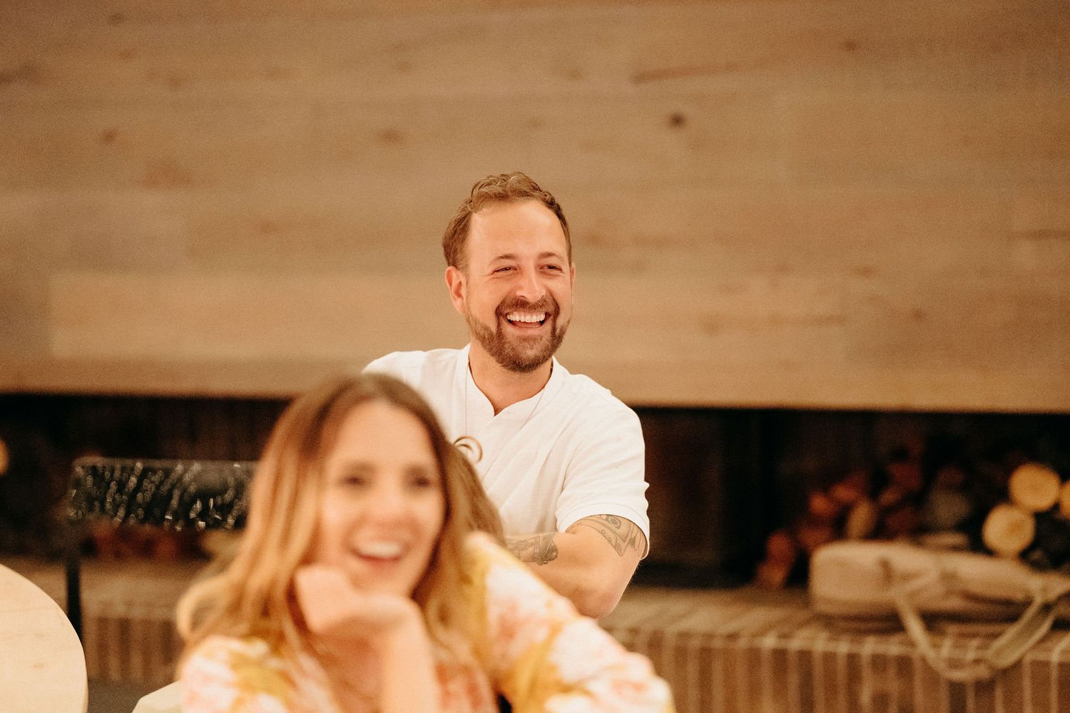 Two people share a joyful moment sitting together in a cozy indoor setting with wooden walls.