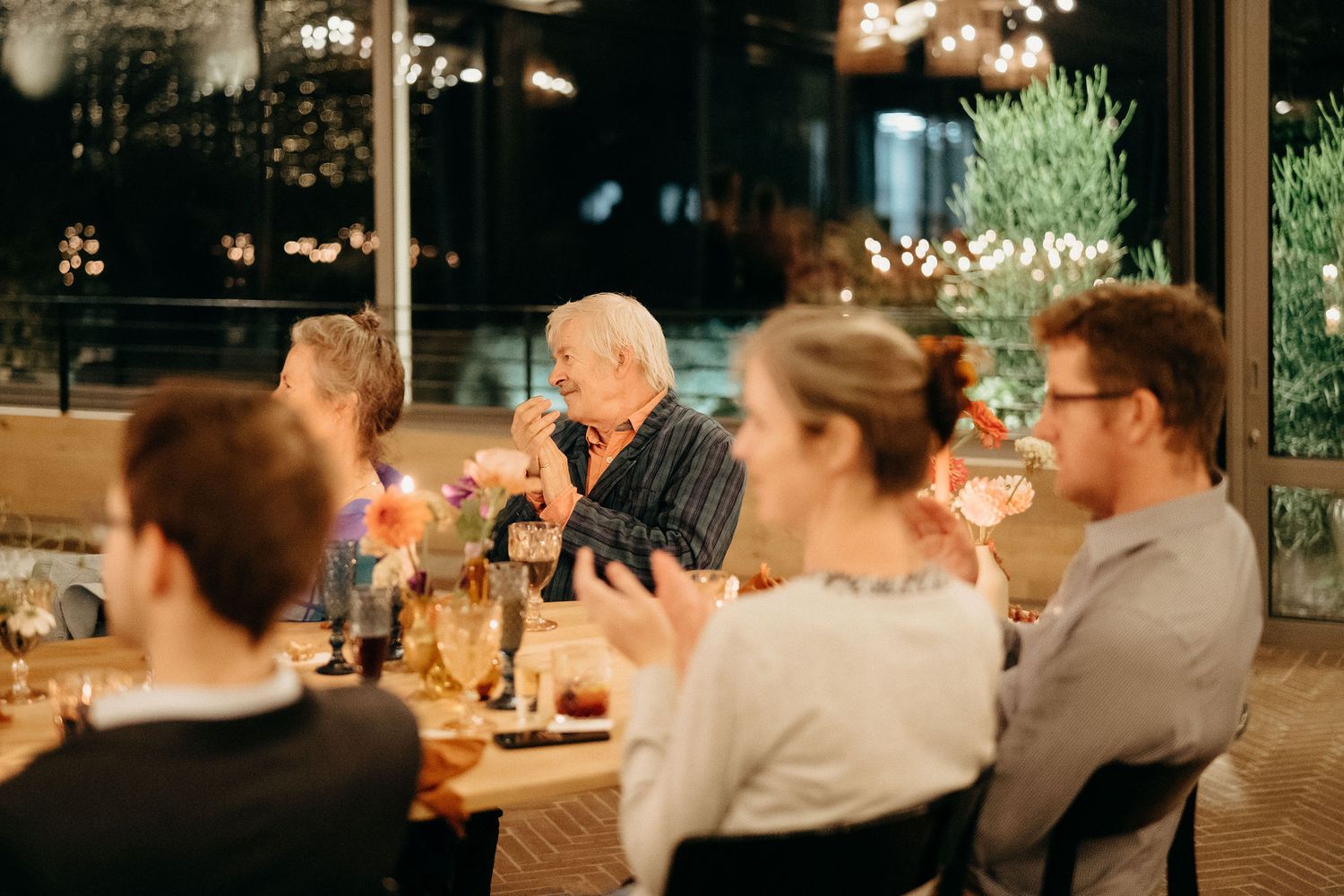 People enjoying dinner at a rustic indoor-outdoor restaurant with warm ambient lighting and table settings at dusk.
