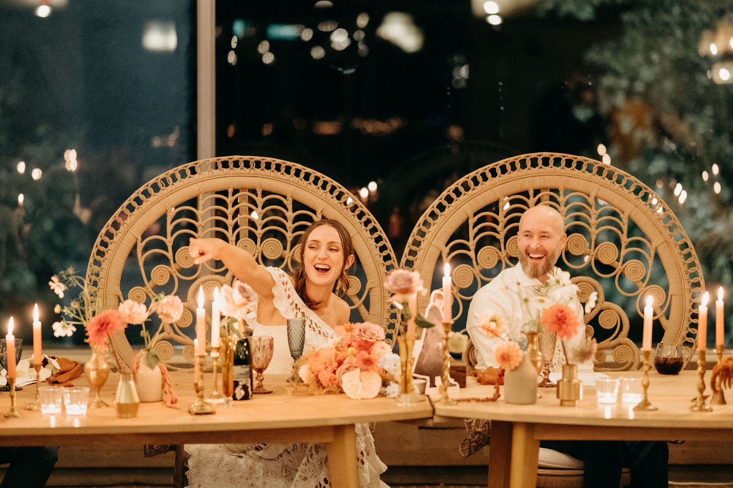 Elegantly decorated wedding reception table with peacock chairs, glowing candles and floral centerpieces at dusk.
