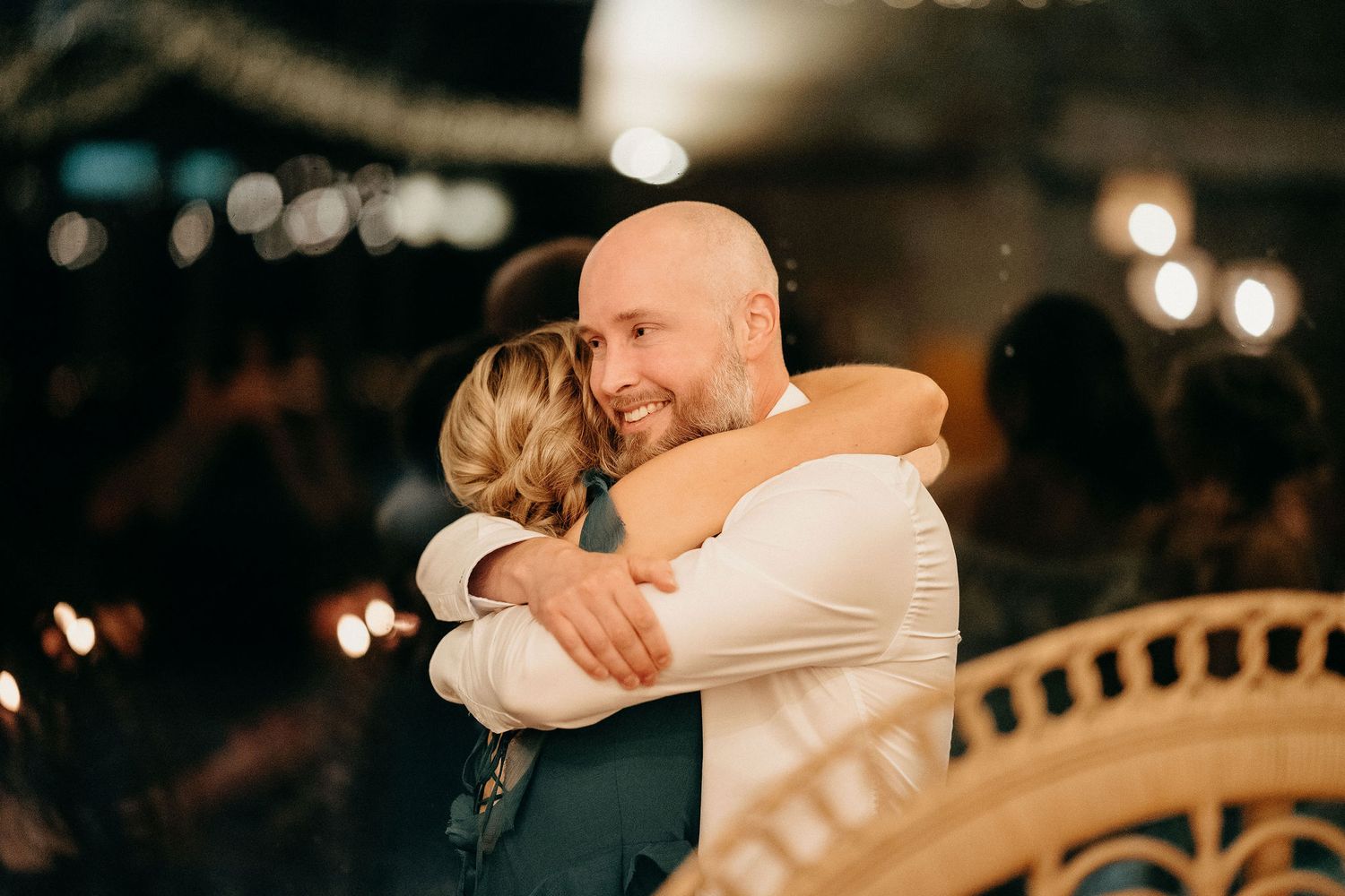 A tender embrace between two people during what appears to be an evening celebration with warm lighting and bokeh effects.
