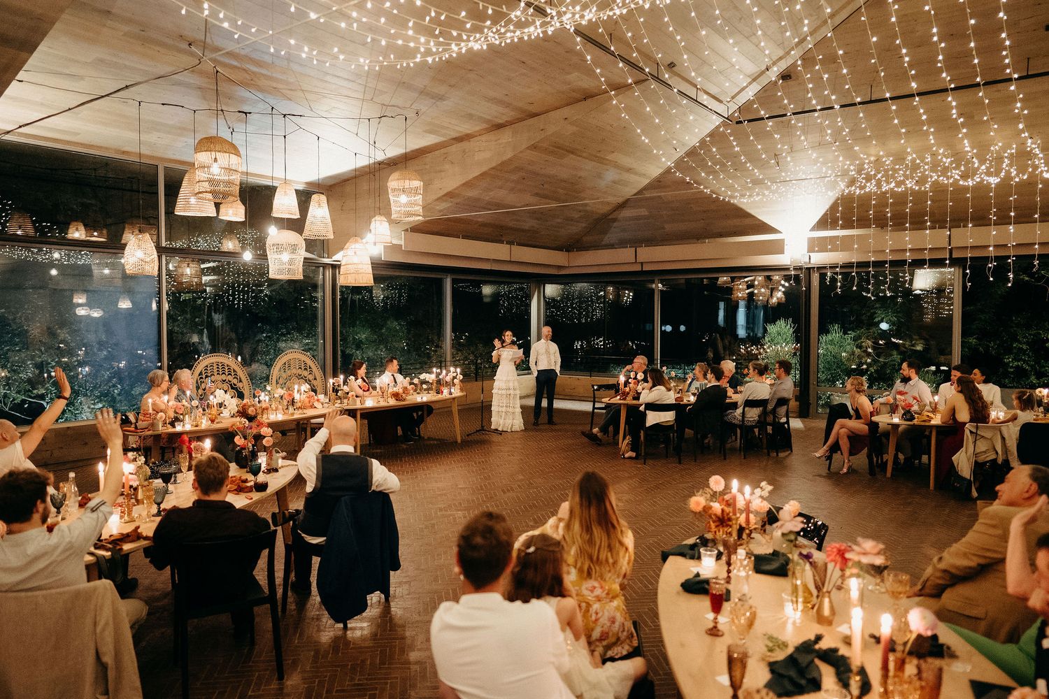Reception guests dine under twinkling string lights in an elegant venue with warm candlelit table settings.
