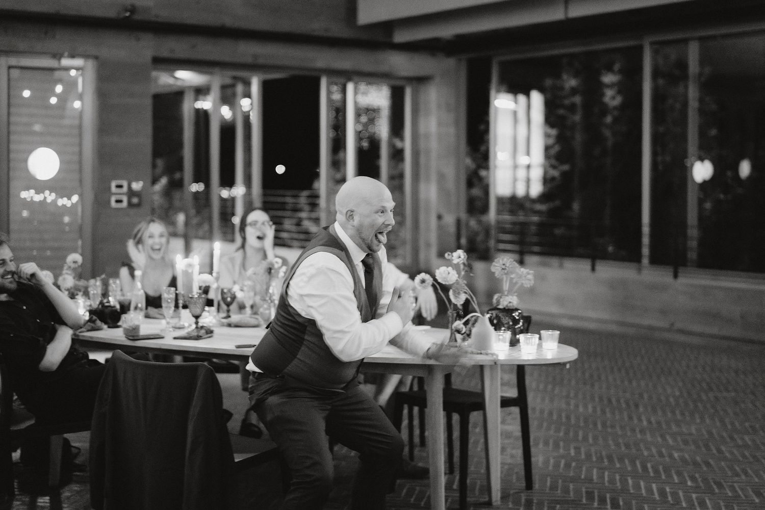 Black and white photo of a server in a vest clearing plates from tables in an elegant dining room setting.