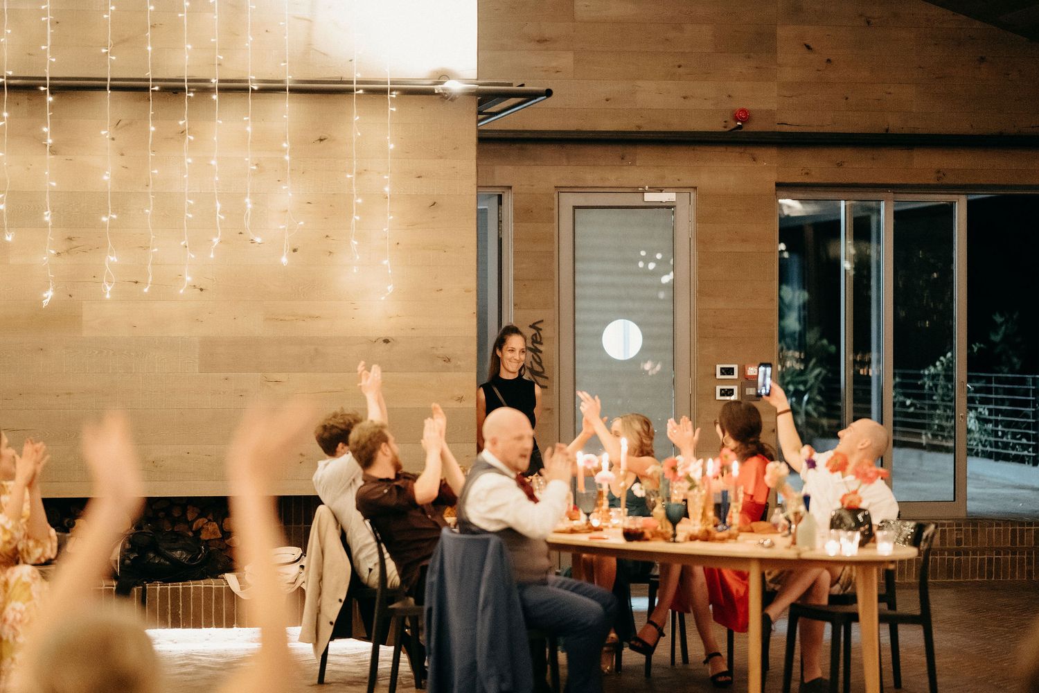 Festive dinner party scene with string lights and candlelit table in an intimate indoor setting.