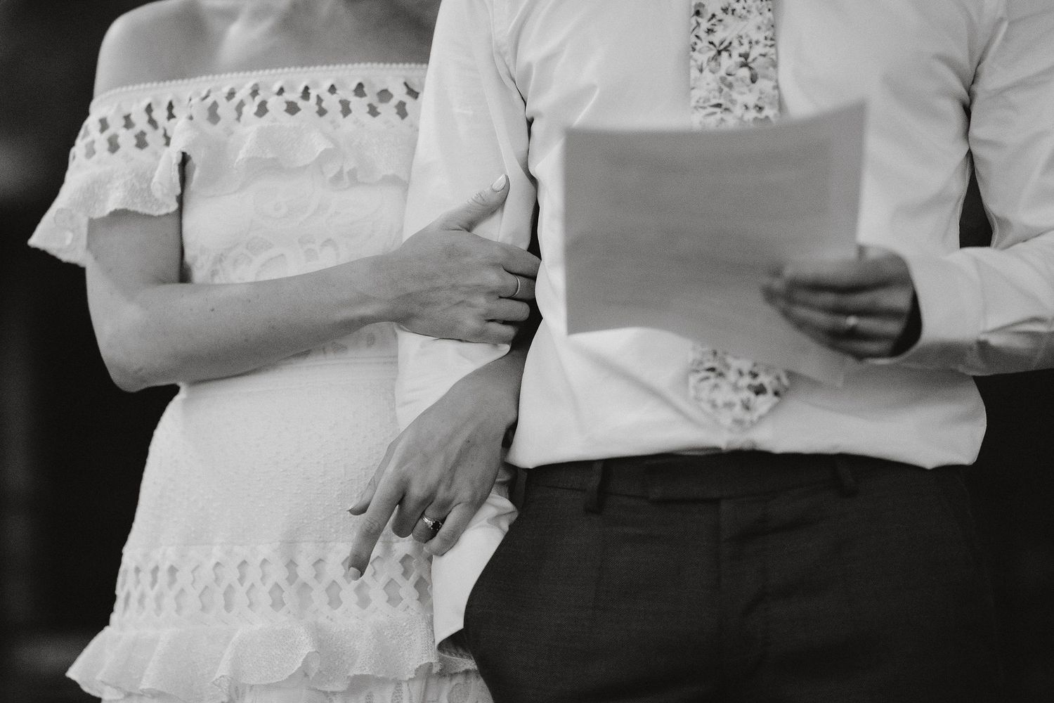 Black and white image of two people holding papers while wearing elegant white lace and formal attire.