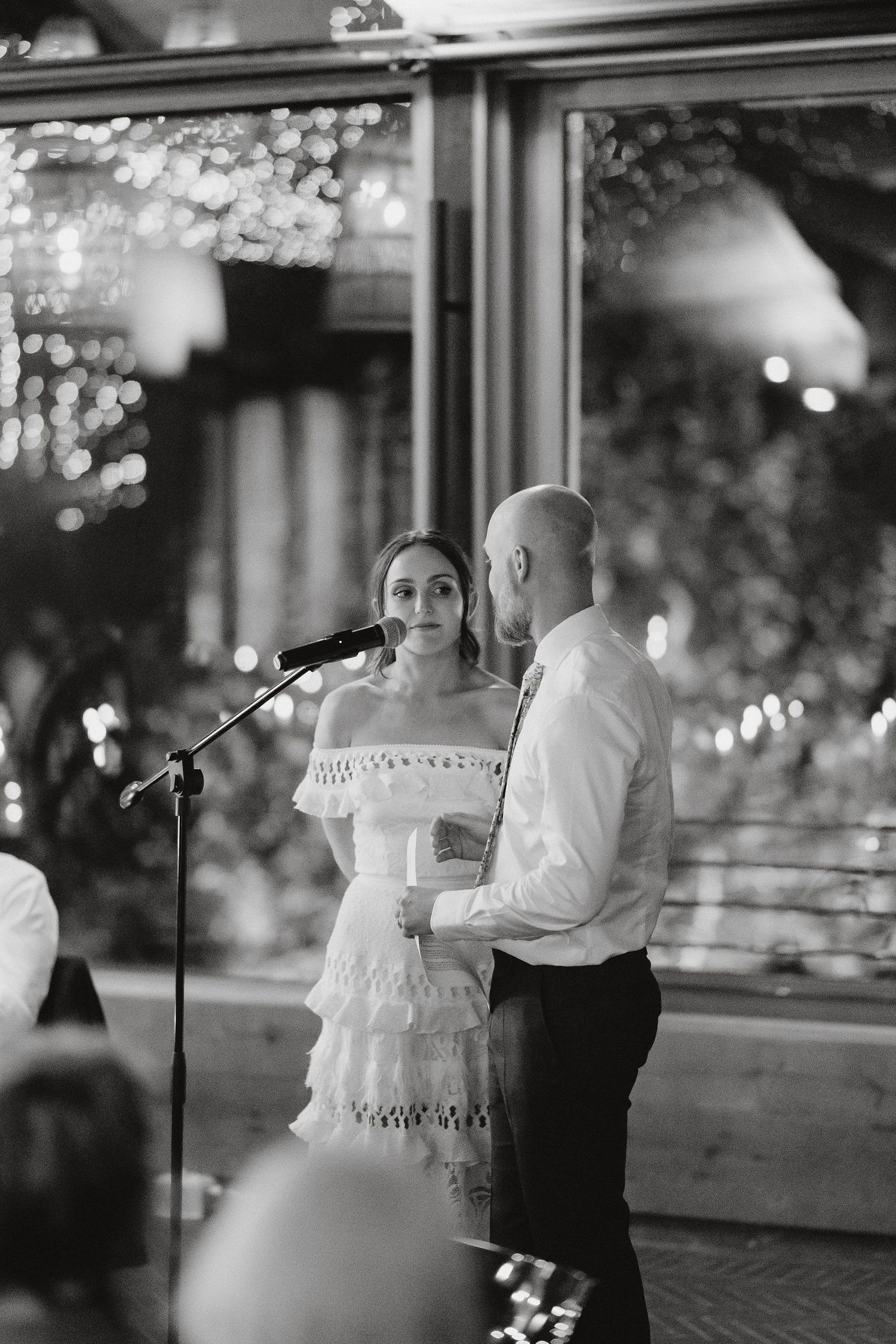 A couple stands together at a wedding reception microphone with sparkling lights in the background.