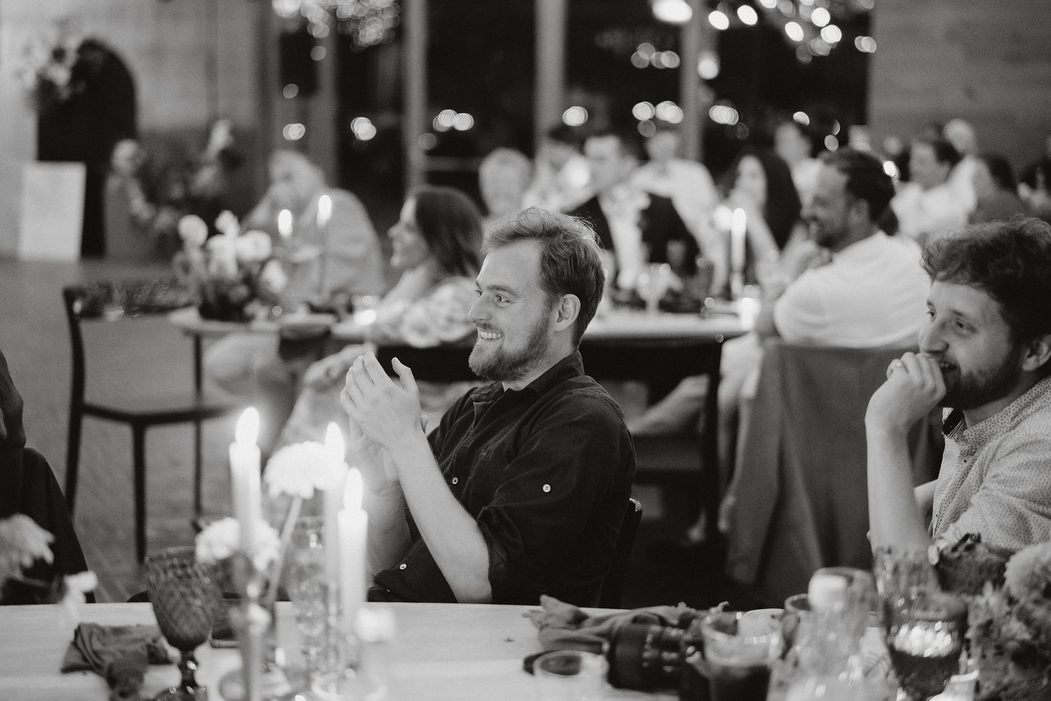 Black and white photo of guests dining and socializing at an evening reception with glowing lights in the background.