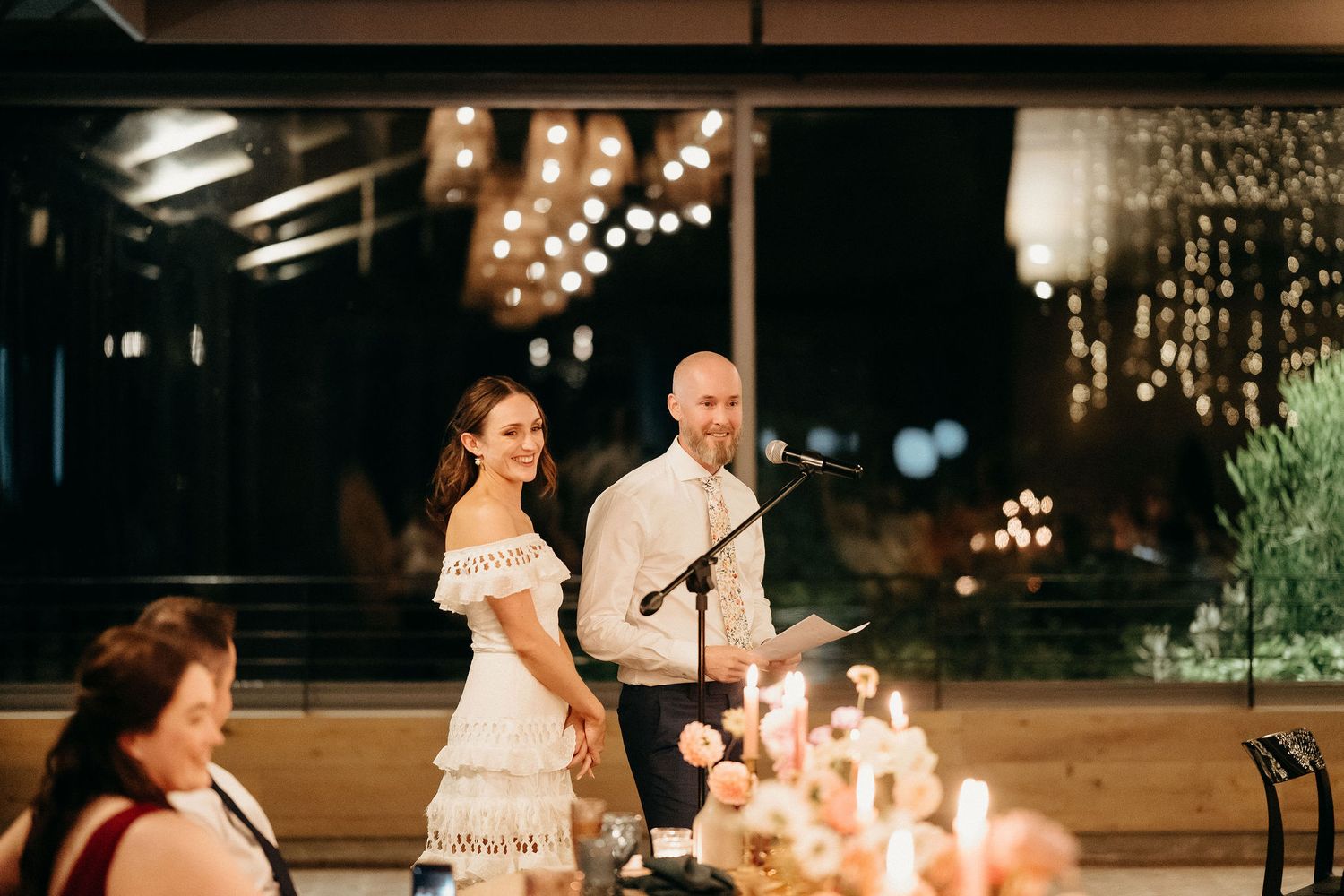 A candlelit reception dinner scene with string lights and decorative elements creating a warm, romantic atmosphere.