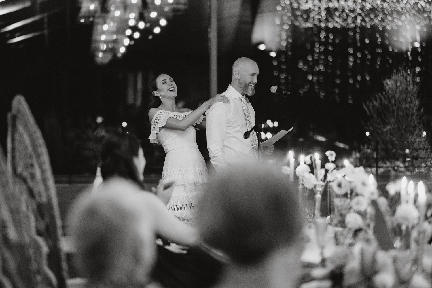 A joyful couple dancing at an elegant evening reception with twinkling lights and chandeliers in the background.