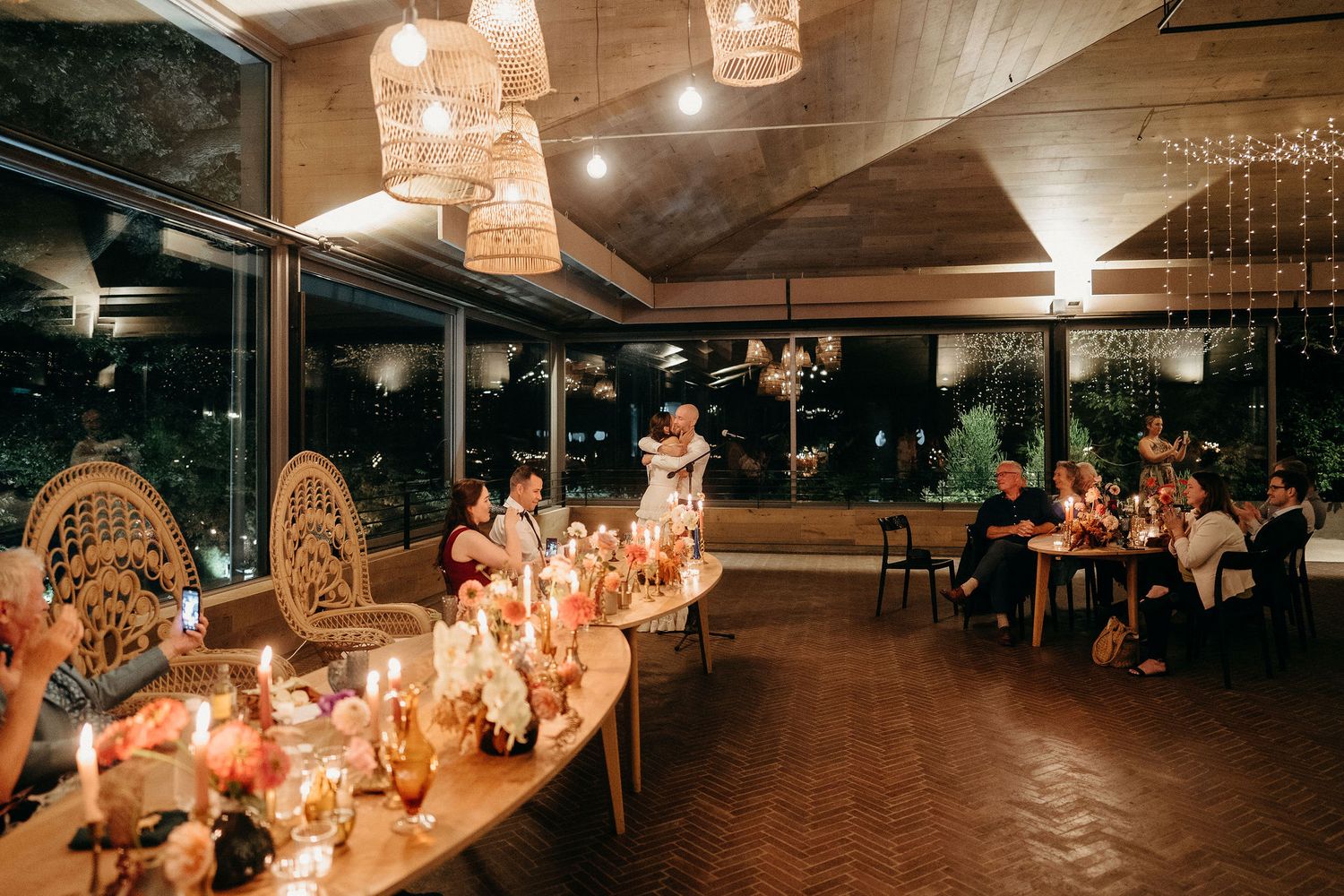 Romantic evening wedding reception venue with candlelit tables, wicker chairs and hanging woven pendant lights.