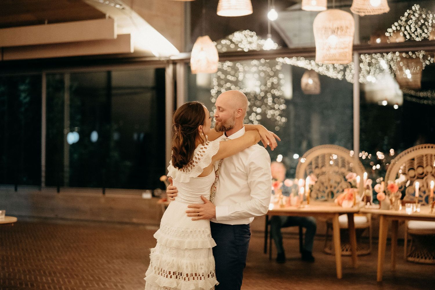 A couple shares a romantic first dance at their wedding reception under warm lighting and decorative string lights.