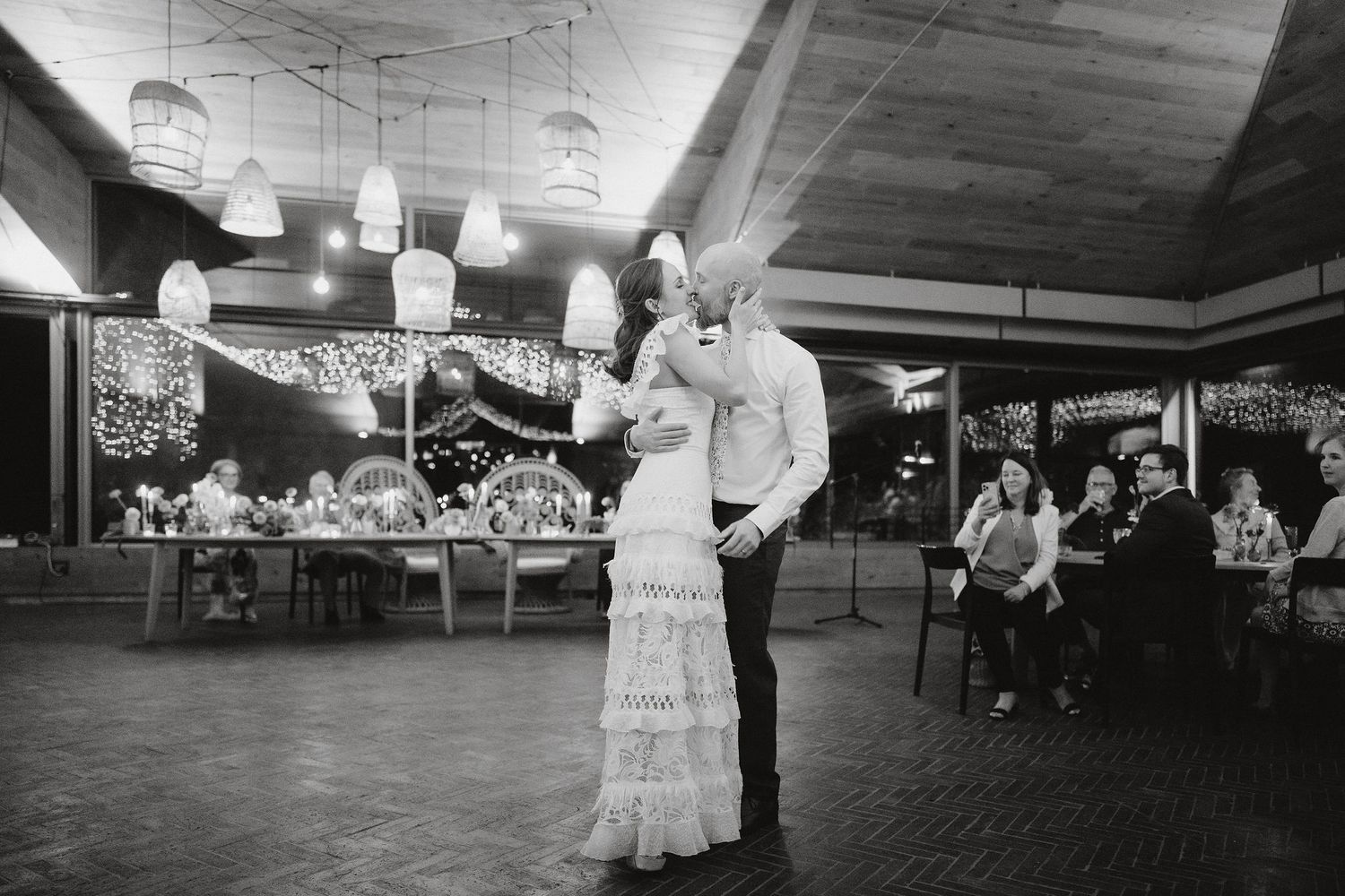 A couple shares their first dance at a wedding reception in a decorated ballroom with black and white photography.