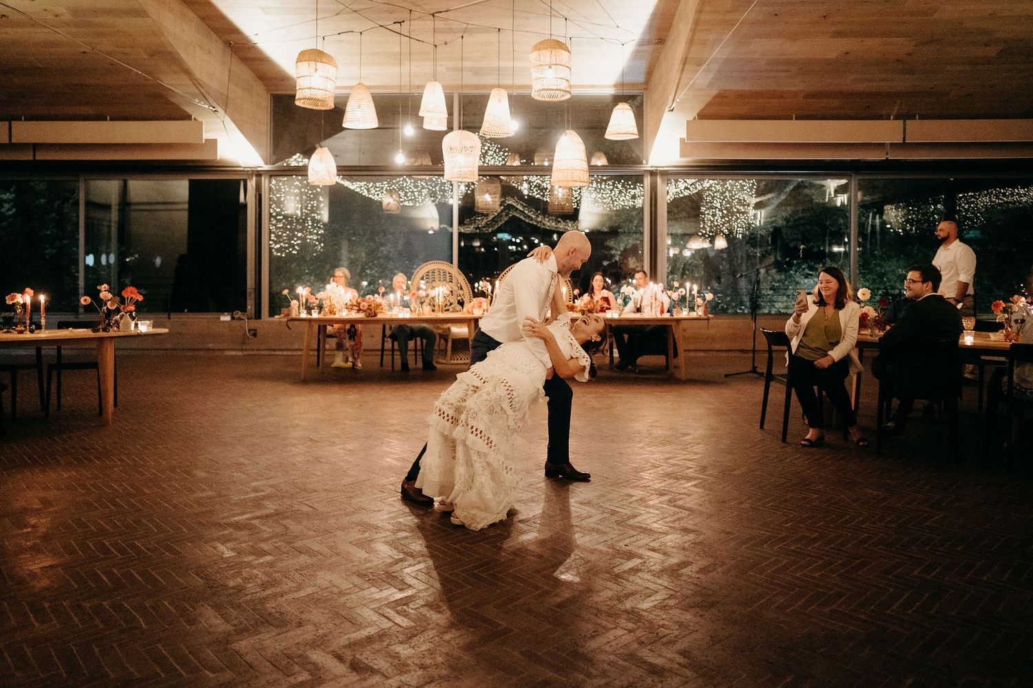 A couple shares their first dance at a rustic indoor wedding reception with warm lighting and wooden details.