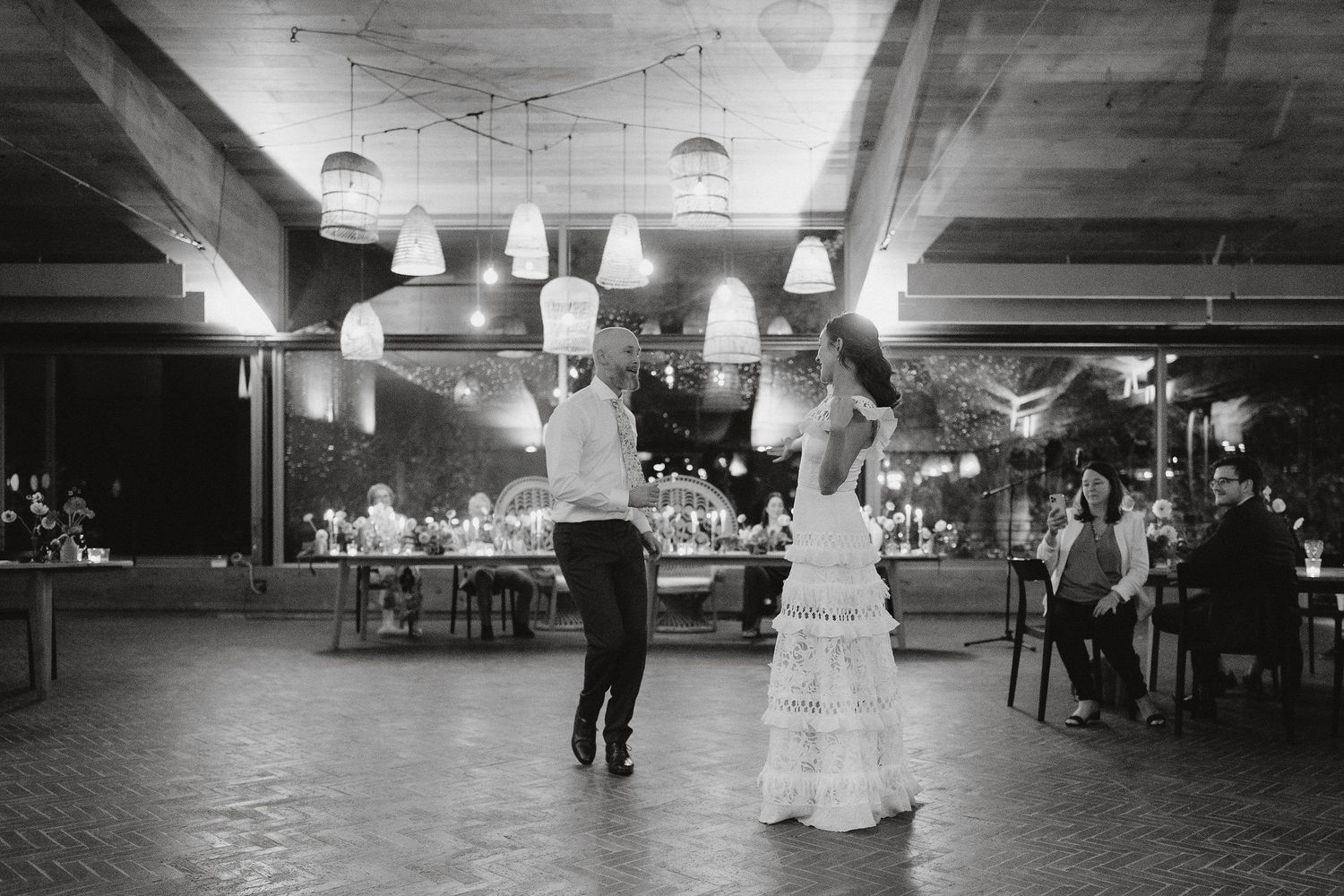 Two people share a dance on a black and white illuminated dance floor at an indoor reception venue.