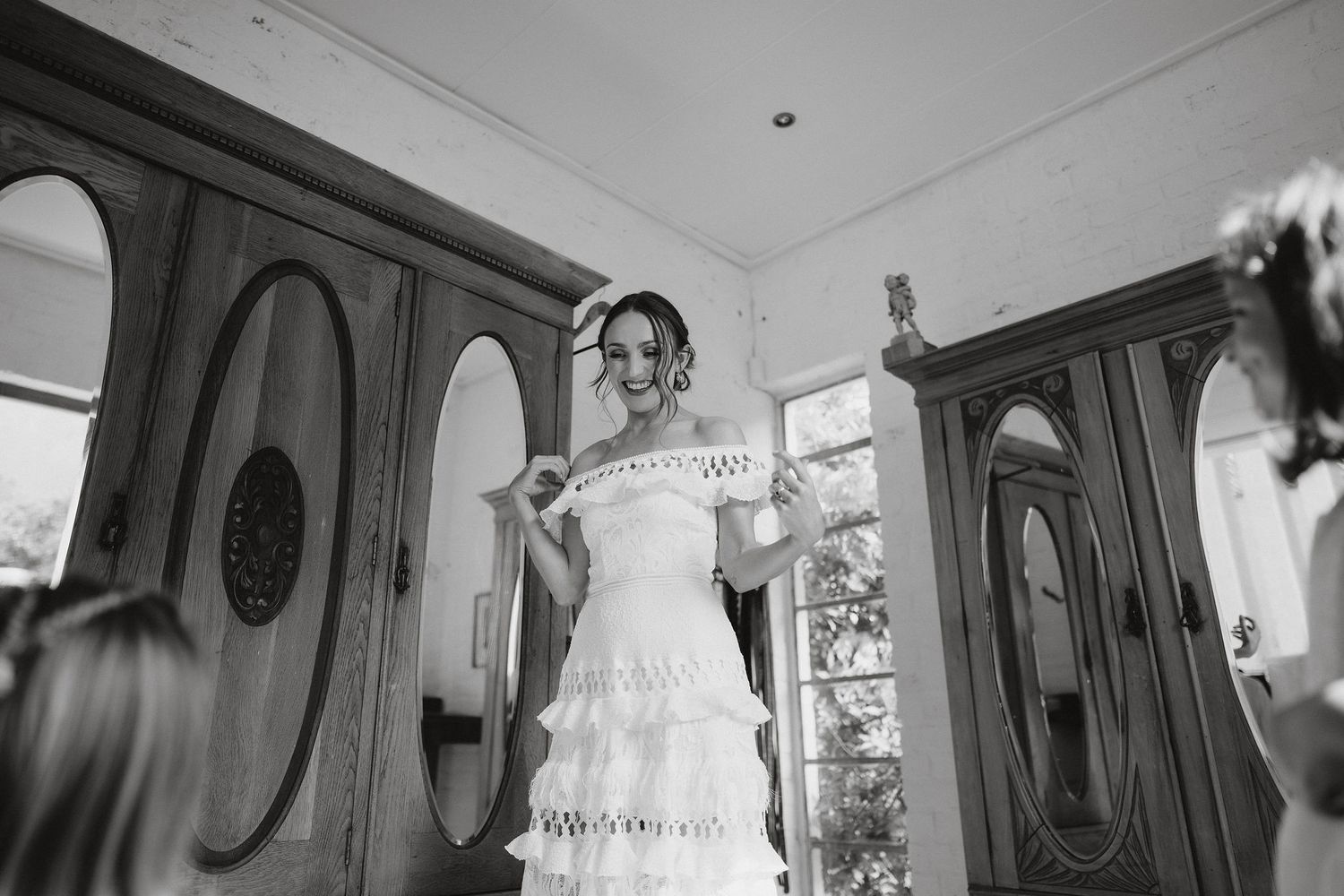A joyful moment captured in black and white as a bride in a white lace wedding dress dances in an elegant room with arches.