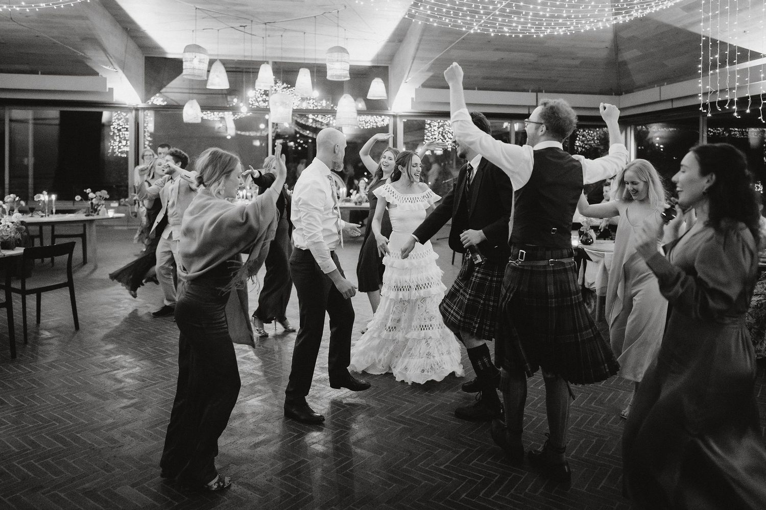 Wedding guests dancing together at a reception venue in black and white on a tiled dance floor.