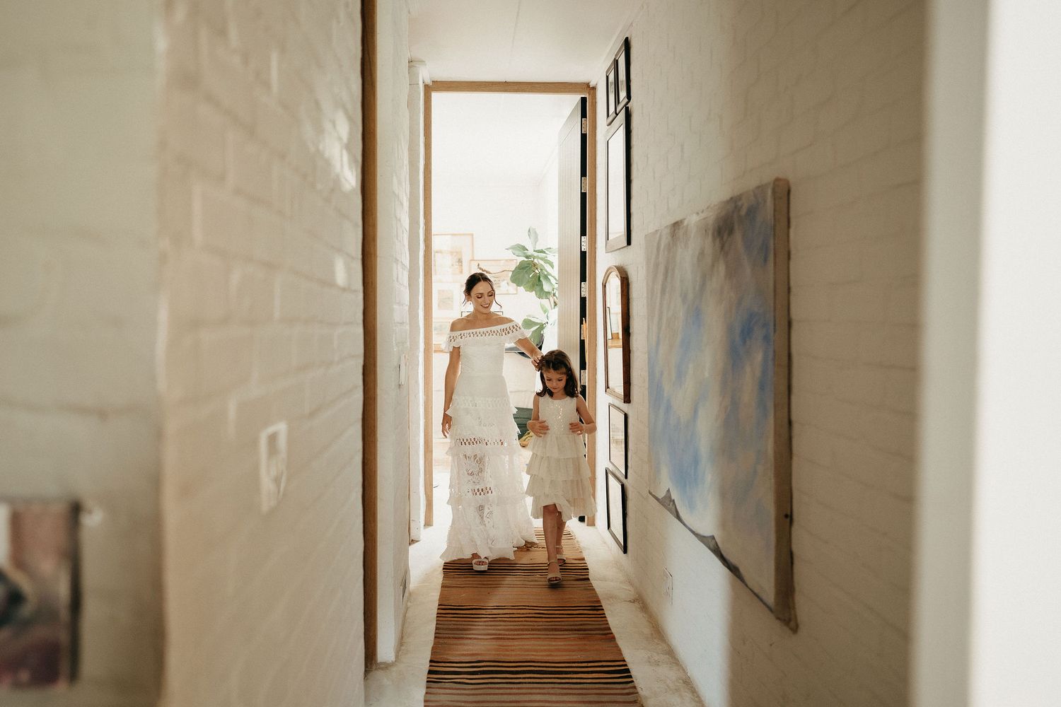 A hallway view showing someone in a white dress standing in a doorway with natural light streaming in.