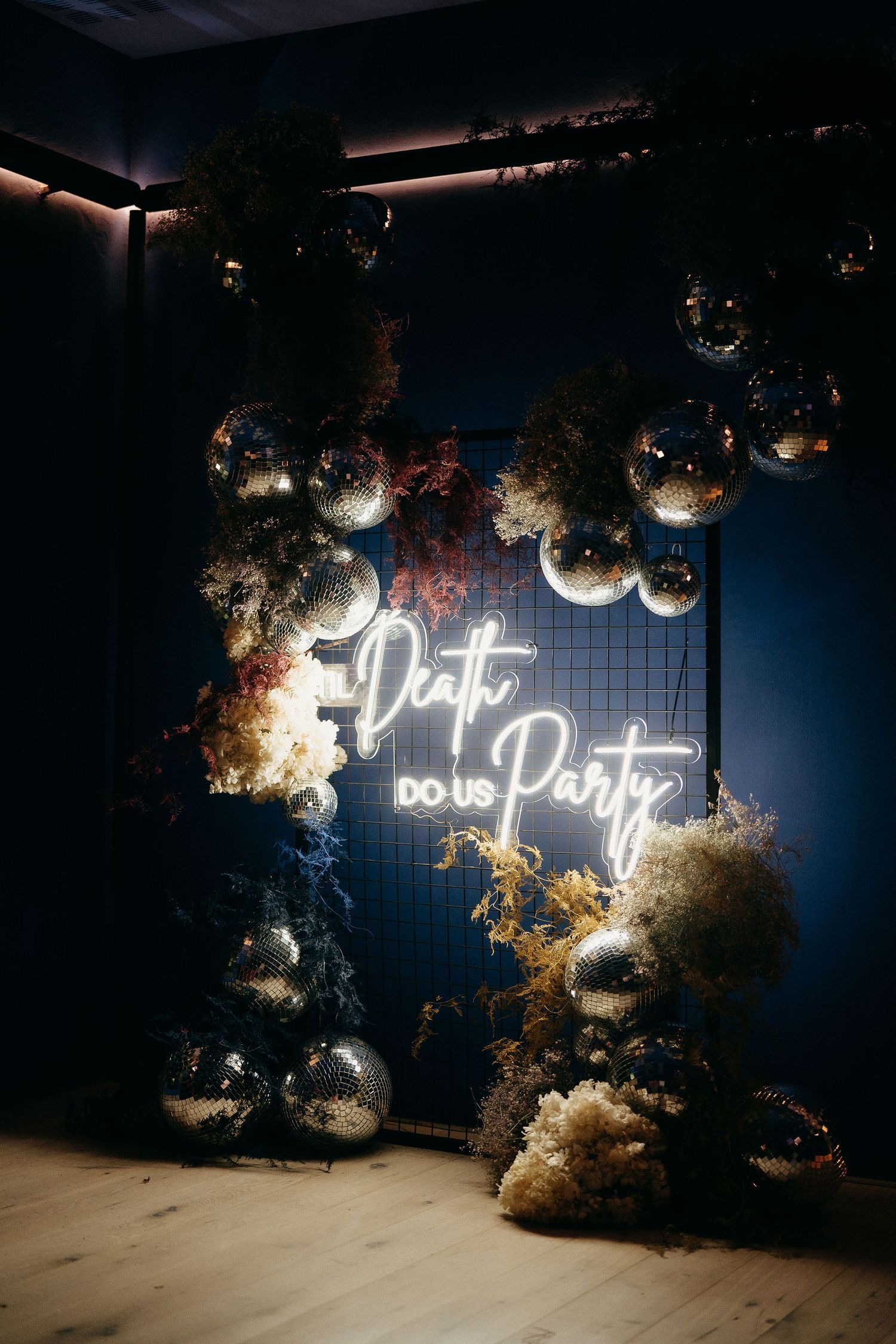Modern party decor featuring a glowing neon "Don't party" sign with silver disco balls and floral arrangements.