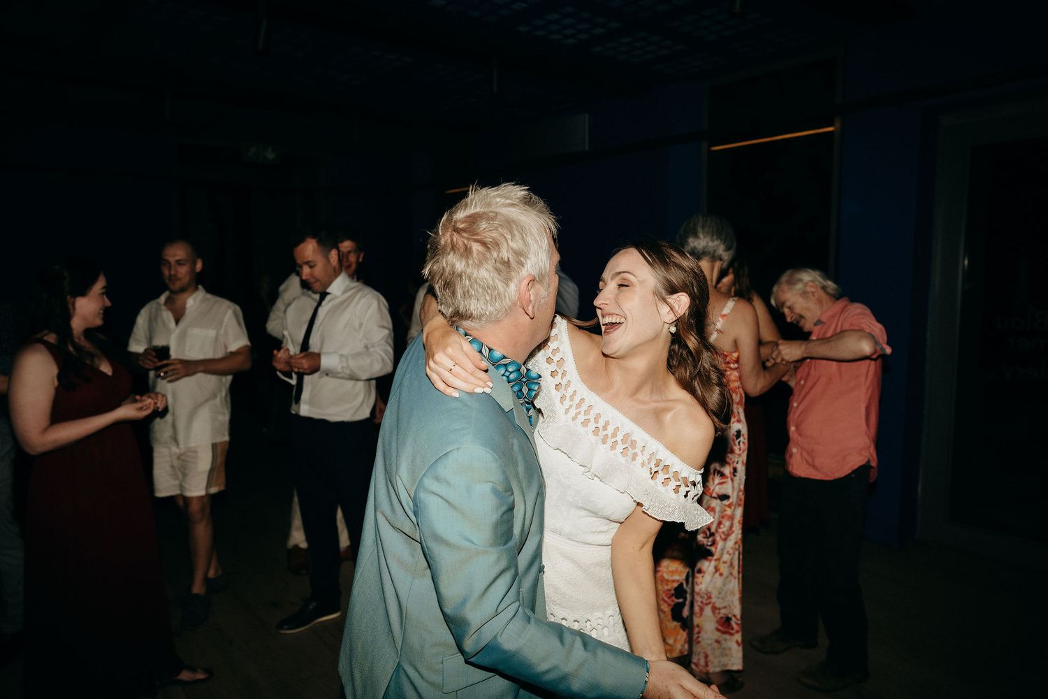 Dancing couple sharing an intimate moment at a wedding reception with guests in the background.