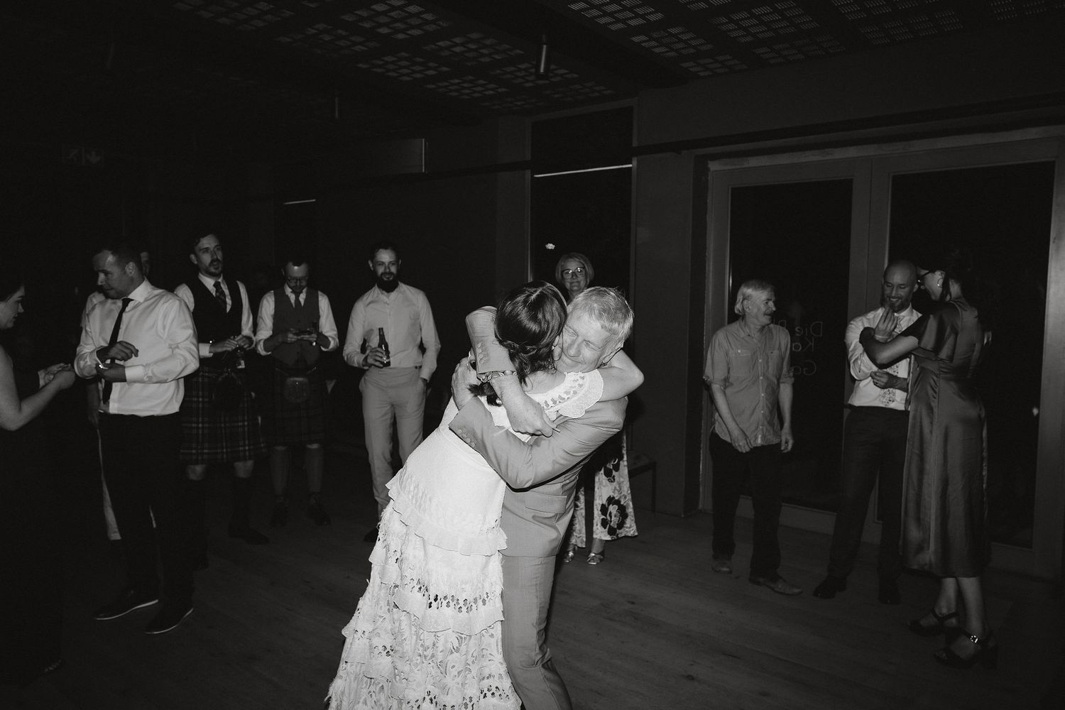 A couple shares a romantic dance at their wedding reception while guests watch on the dance floor in black and white.