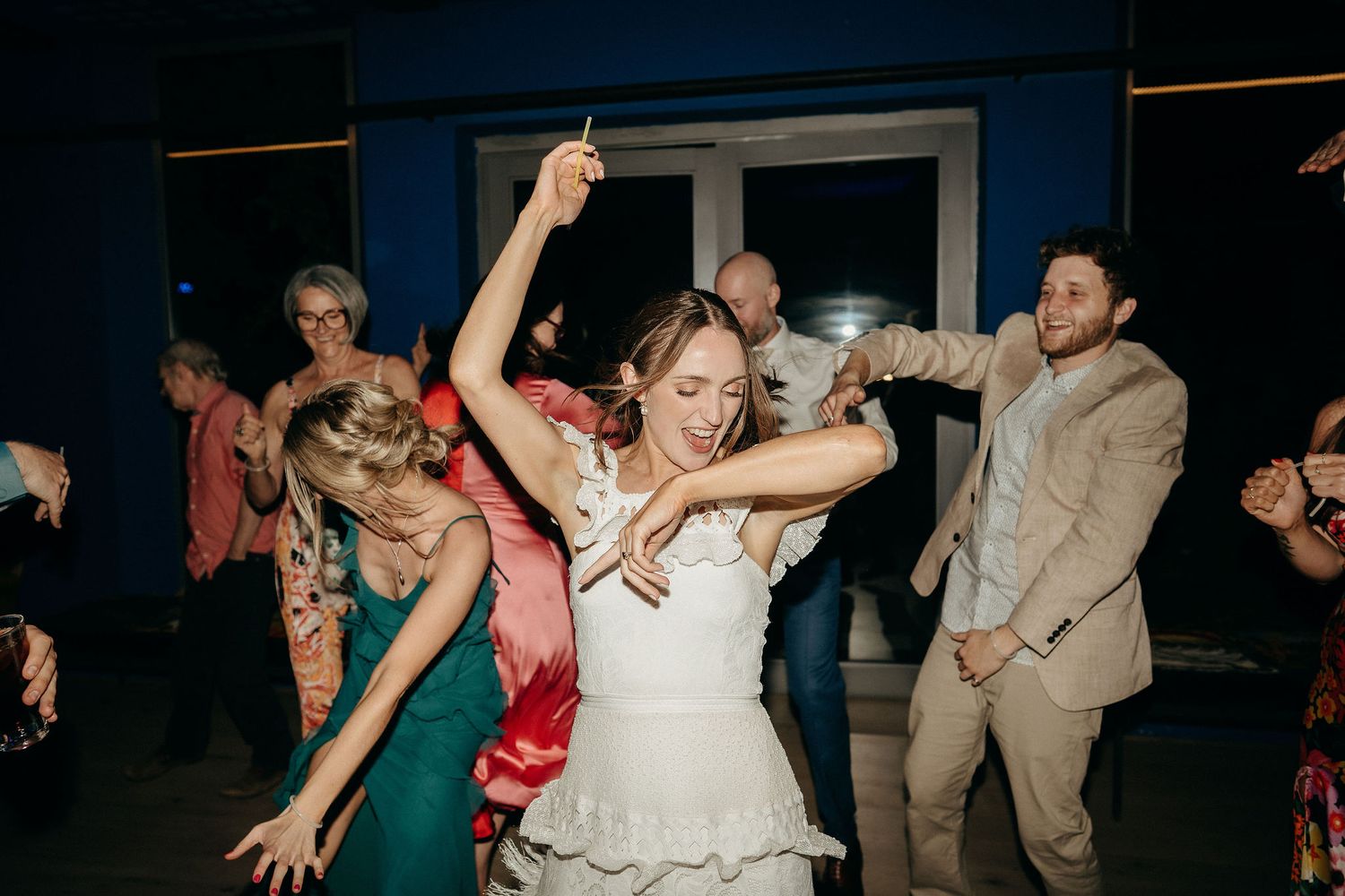 People dancing enthusiastically at a wedding reception with the bride in a white dress at the center of the dance floor.