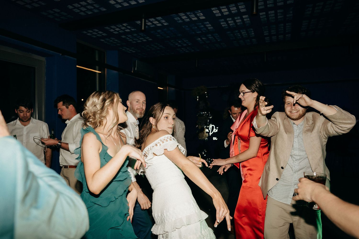 Wedding celebration with people dancing and enjoying themselves on a dark dance floor at a reception venue.