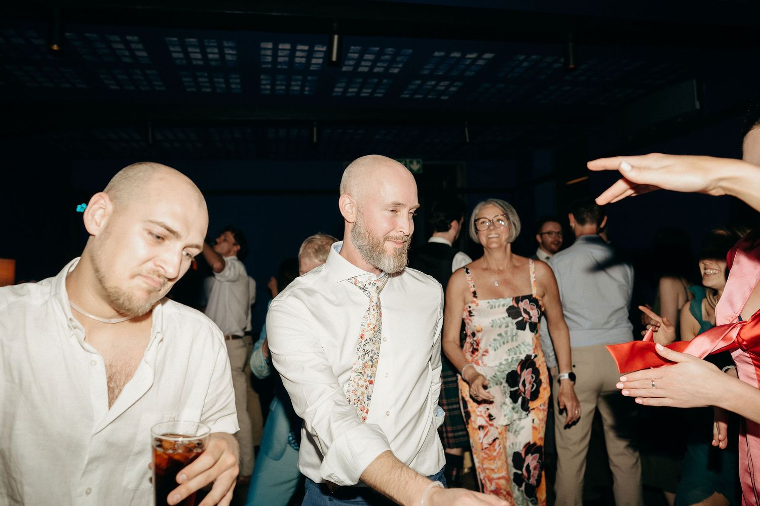 People dancing and socializing at a dimly lit indoor party or reception venue.