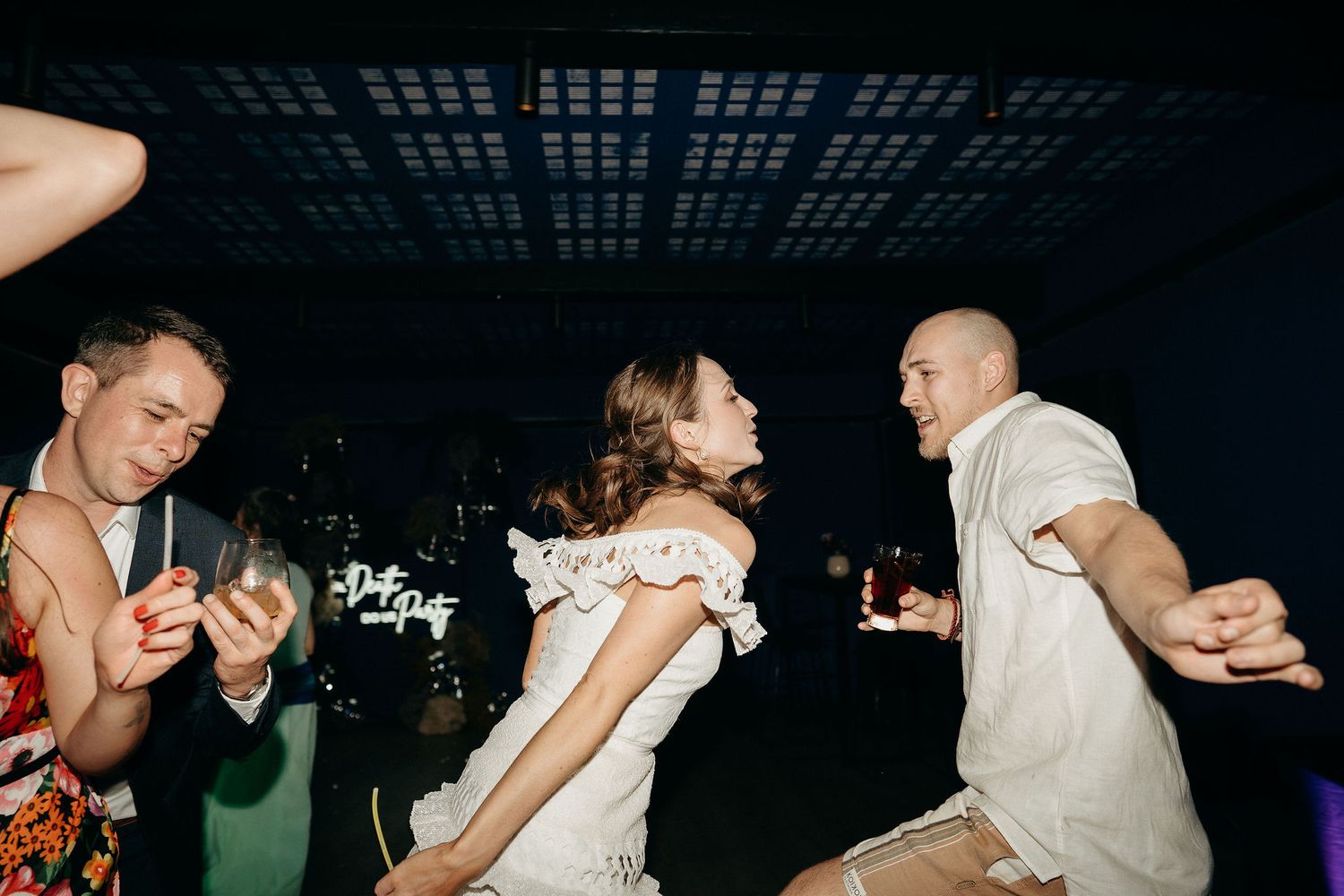 Wedding guests dancing energetically on a dark dance floor during a reception celebration.