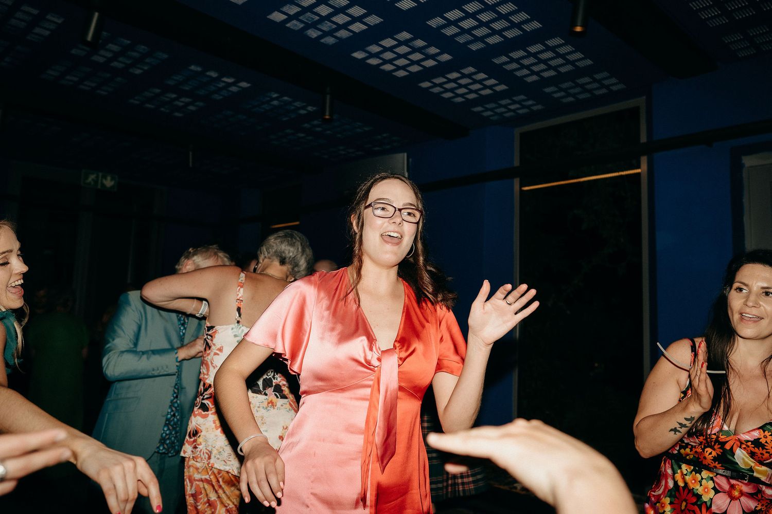People dancing in a dimly lit nightclub with a coral-colored dress visible in the foreground.