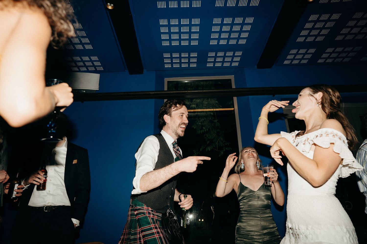 Guests dancing and celebrating energetically at a wedding reception with a blue ceiling.