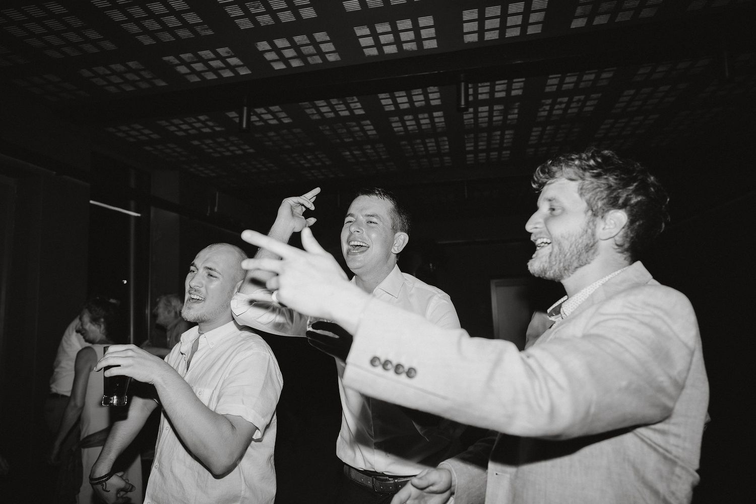 Three men share drinks and laughs together at what appears to be a celebration in a vintage black and white photograph.