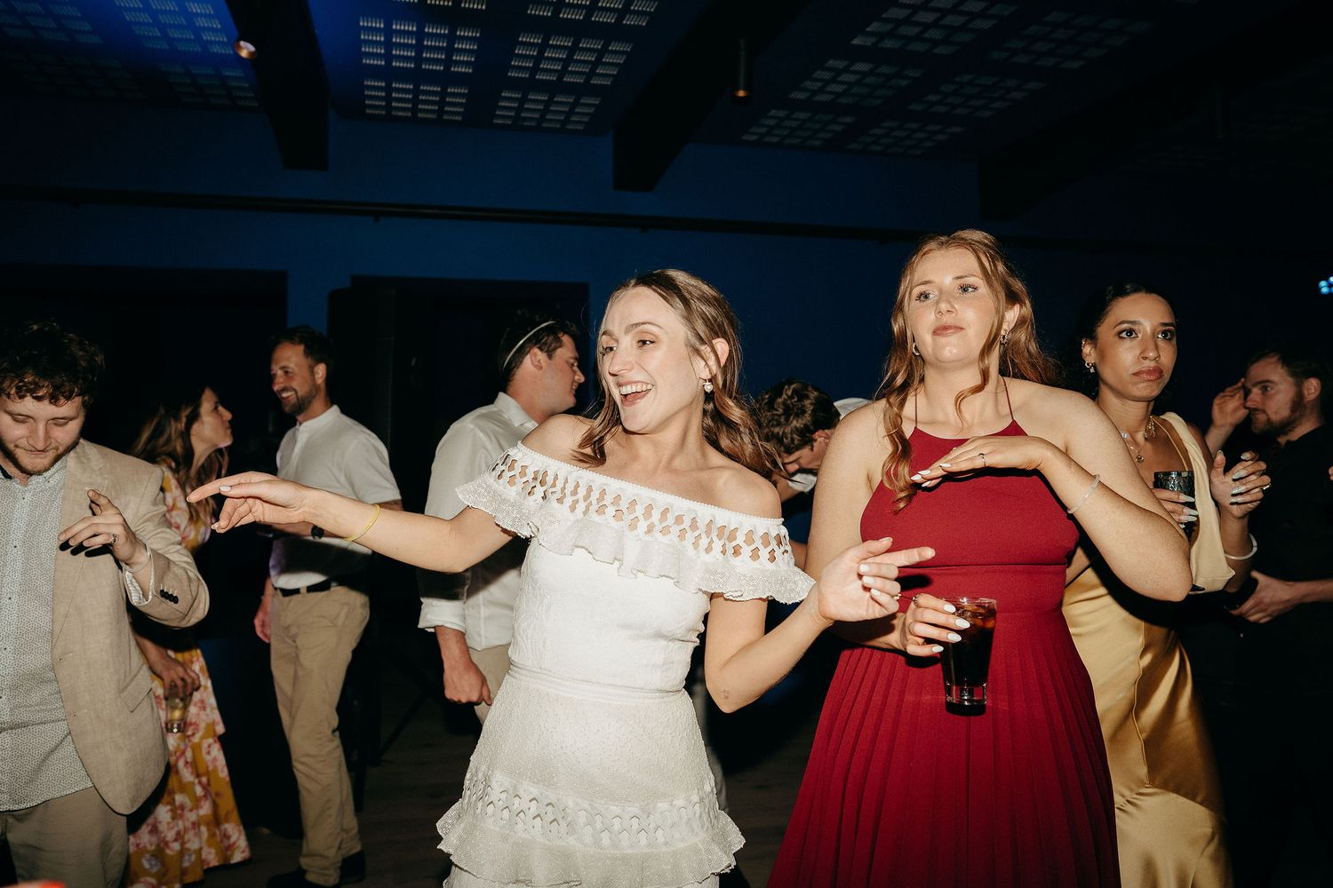 People dancing enthusiastically at a wedding reception with someone in white and another in red enjoying the celebration.