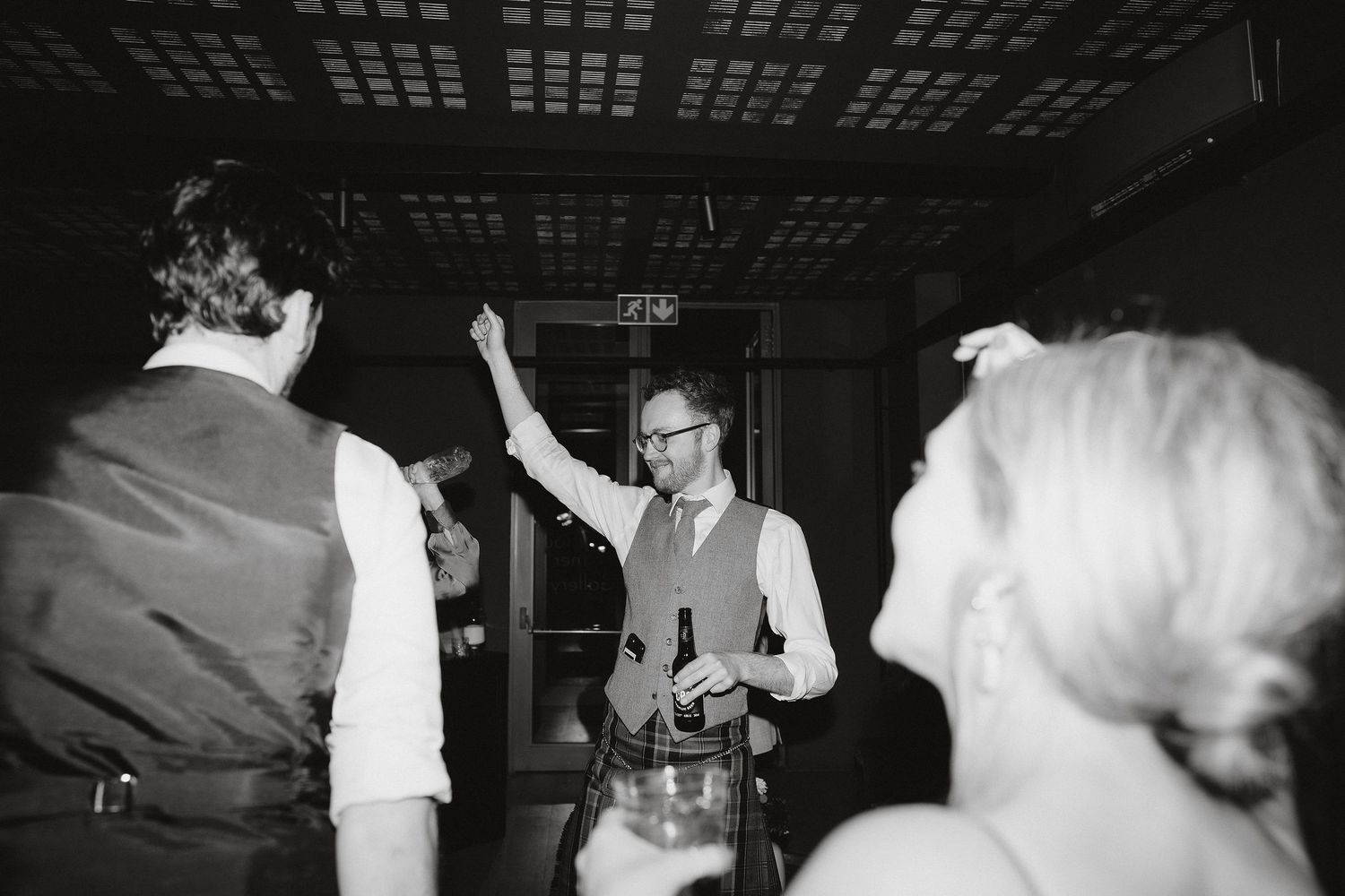 A black and white photo of people dancing and celebrating at a party in an indoor venue.