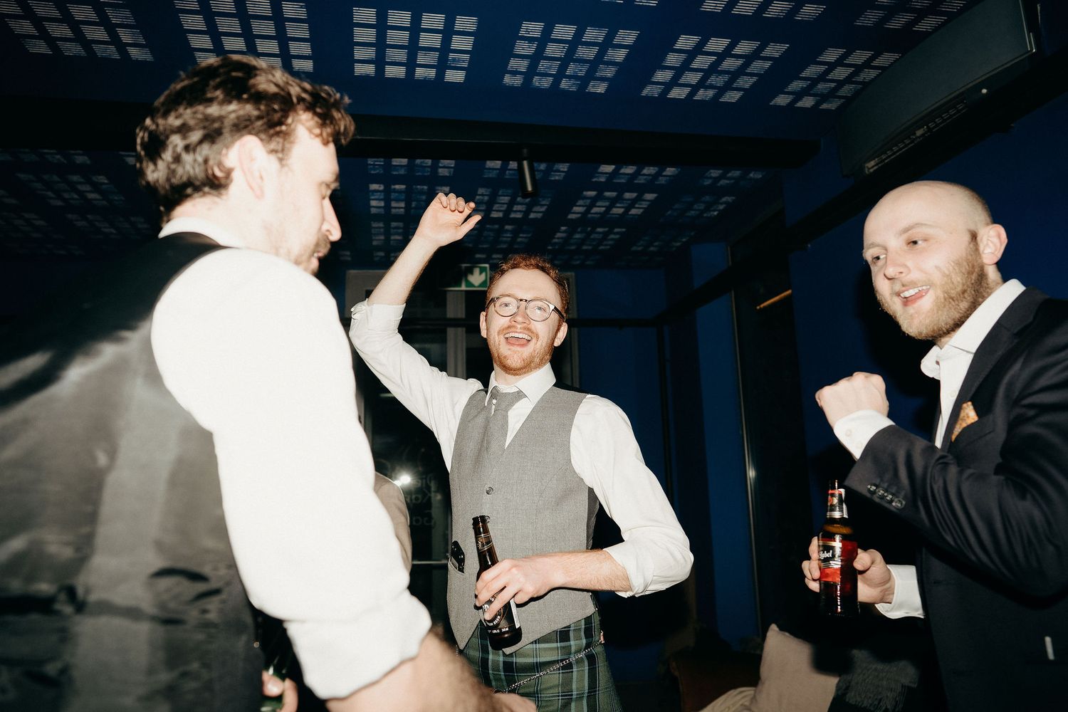 Three people at a nighttime event share laughs and drinks while enjoying themselves in a dimly lit setting.