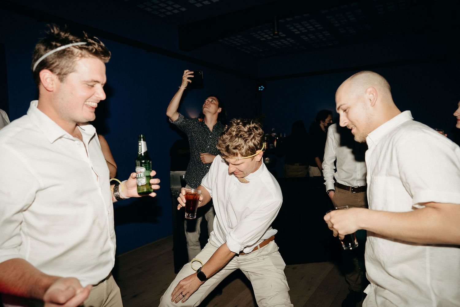 People dancing and enjoying themselves at a party event with white shirts and dark background.
