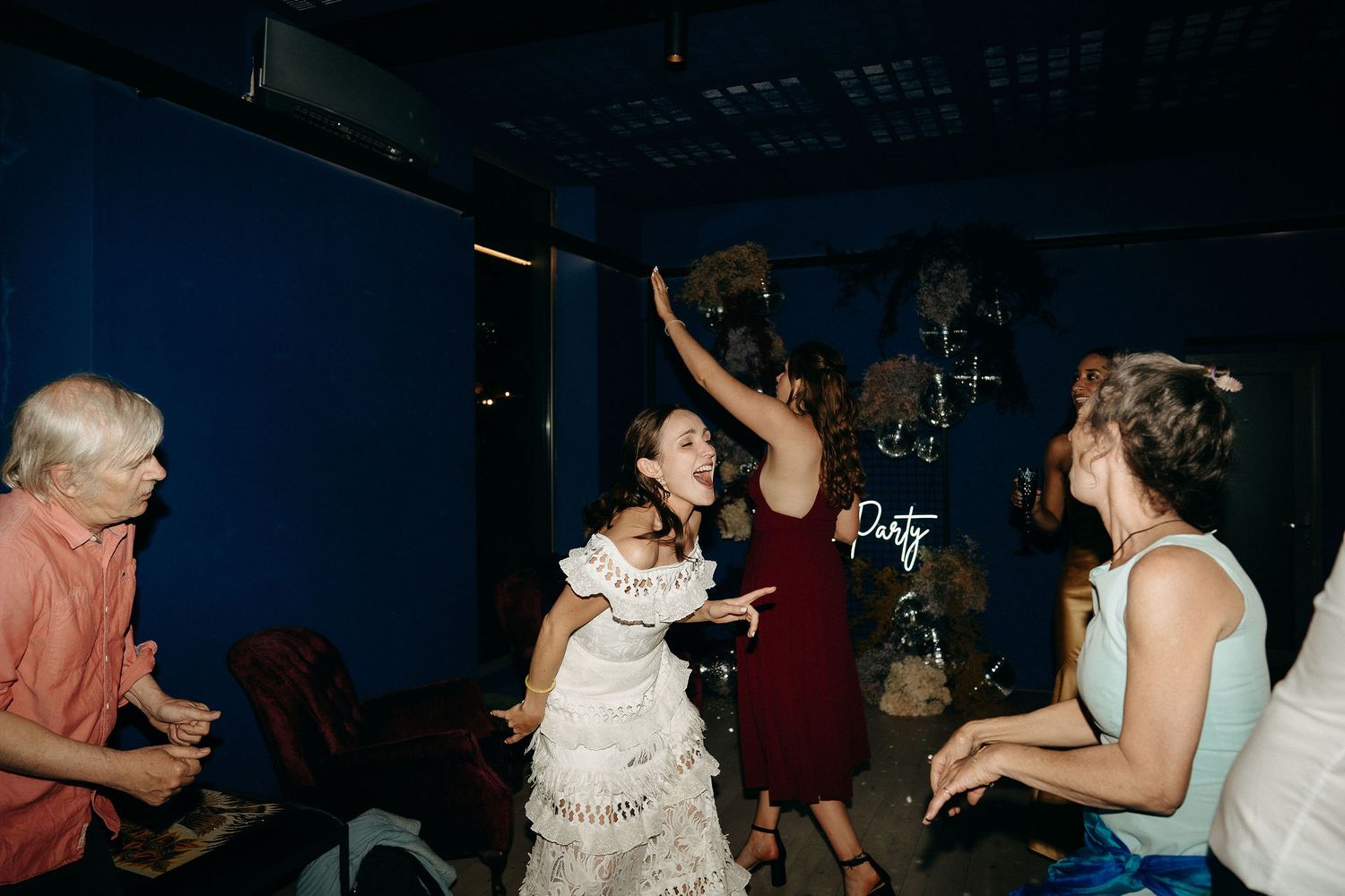 People dancing and celebrating at a party with one person in a white dress and another in a dark dress.