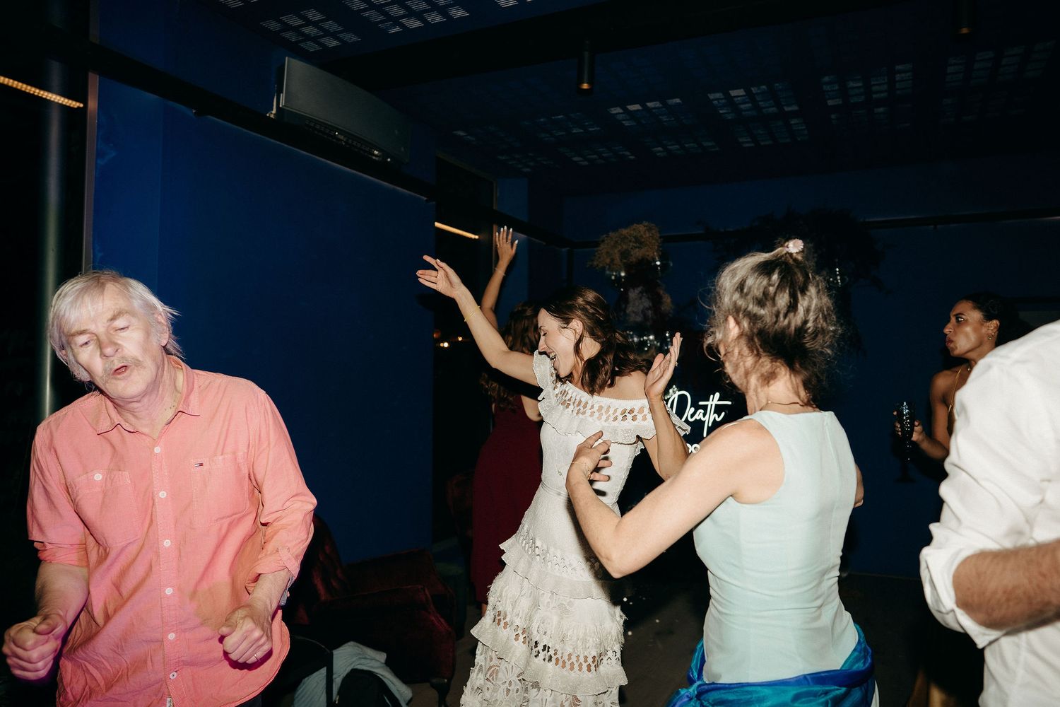 People dancing and having fun at a lively indoor party with blue walls visible in the background.