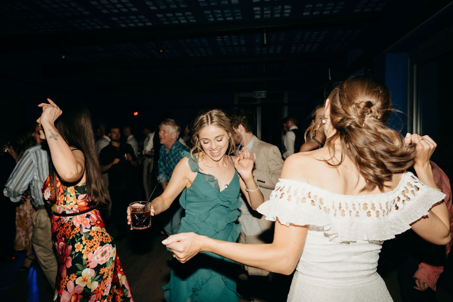 Party guests dance together on a dimly lit dance floor with a playful and energetic atmosphere during an evening celebration.
