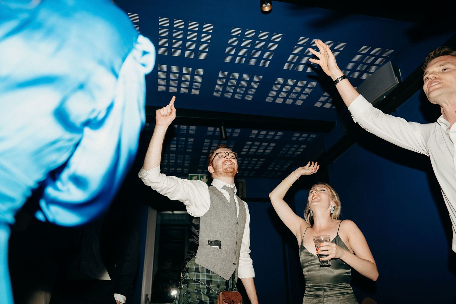 People dancing enthusiastically under blue lights at a nightclub party.