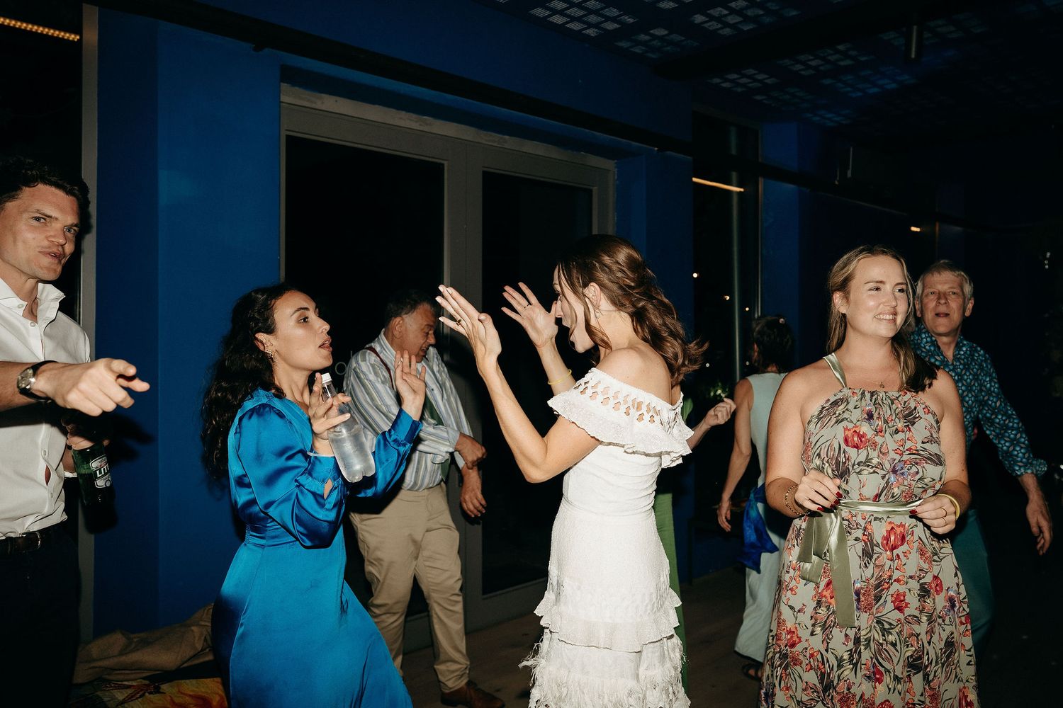 Wedding guests dance and celebrate enthusiastically at a nighttime reception with blue lighting.