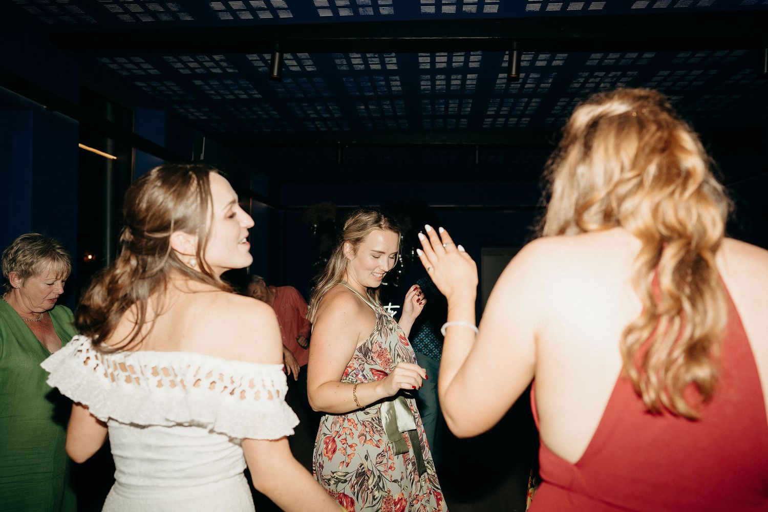 People dancing and socializing at a dimly lit indoor party venue with casual and formal attire.