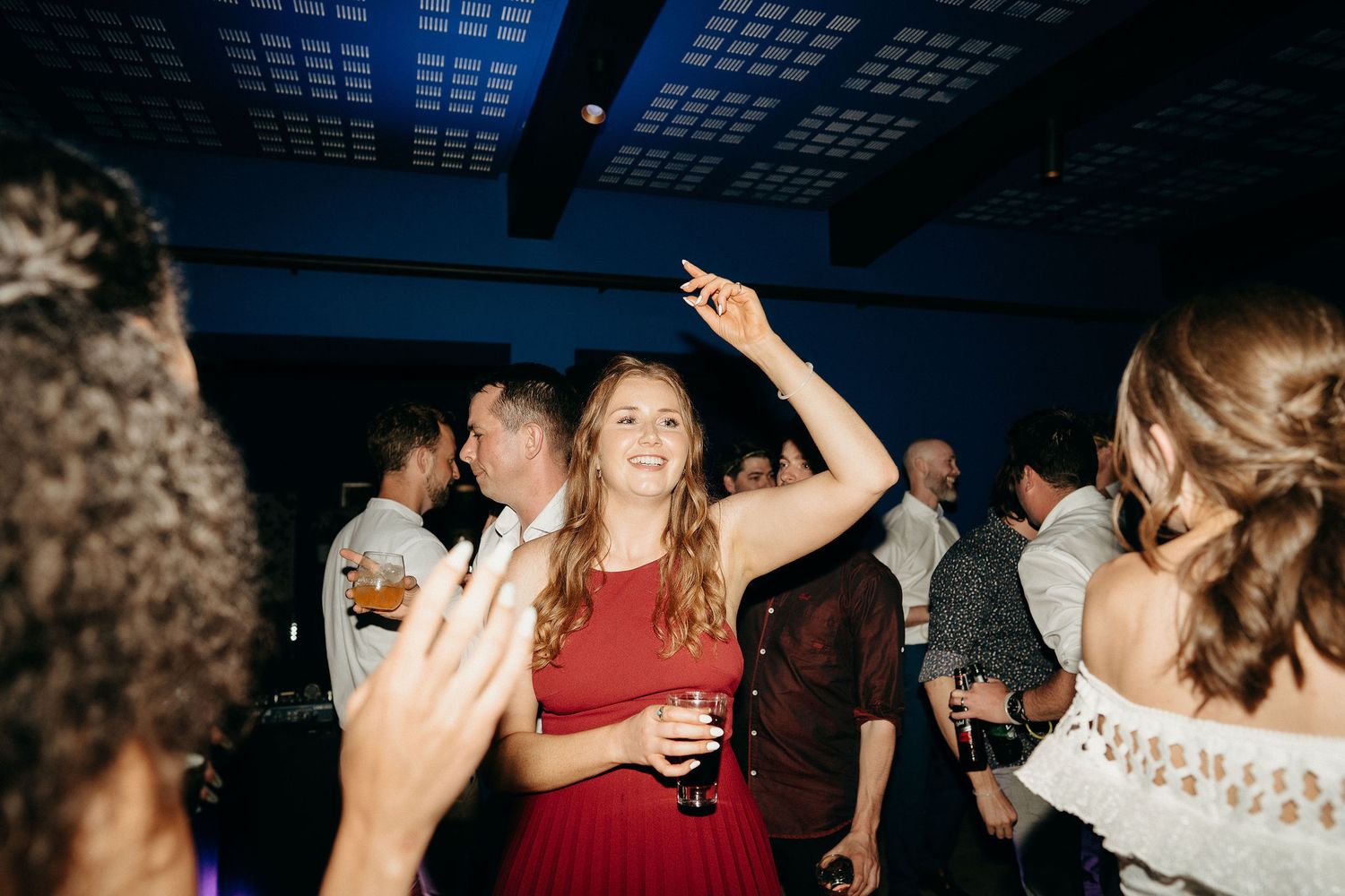 People dancing and having fun at a nightclub with blue lighting and drinks in hand.